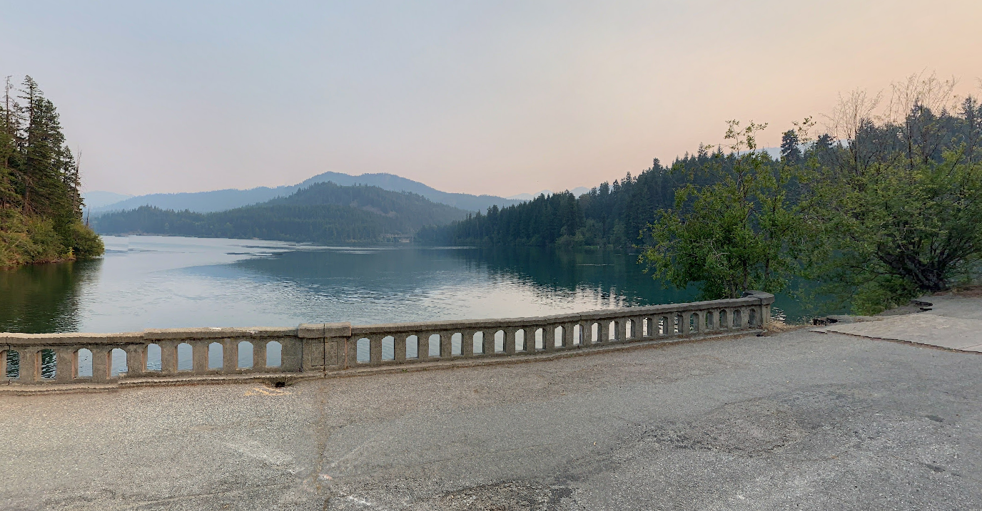 Hazy panoramic view of a lake, forested hills, and a stone railing.