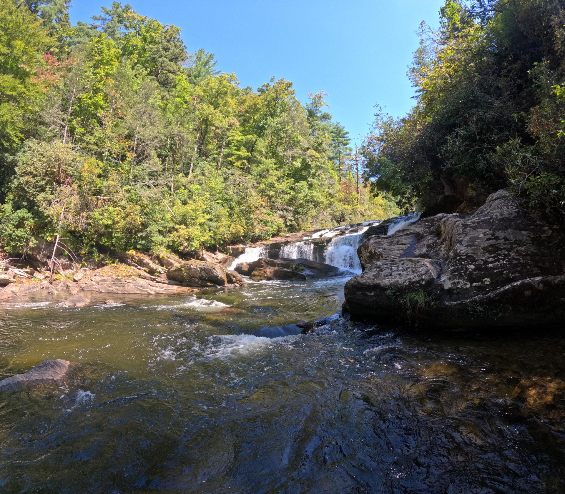 A wide river with cascading waterfalls and rocky banks under a blue sky.