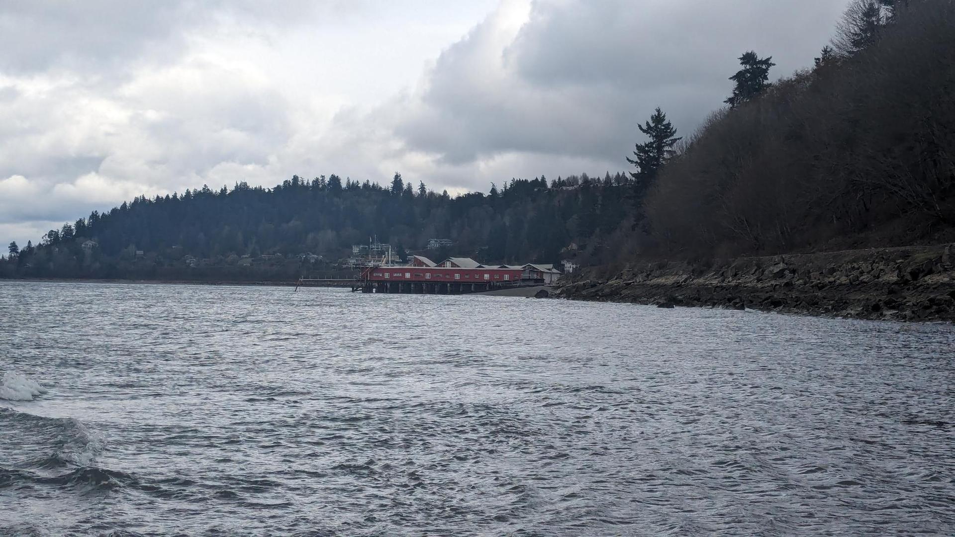 Overcast view of water, a red building, and a forested hillside.