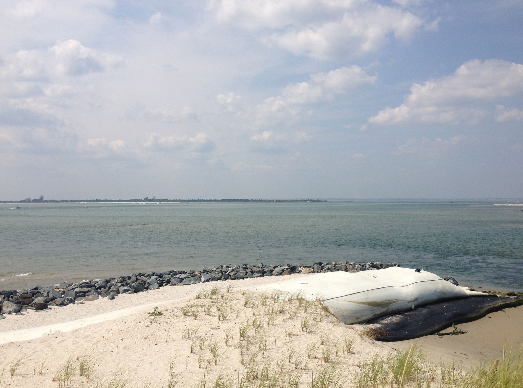 Sandy beach with a large white object and rock barrier by calm ocean. - Viewpoint loop from Sedge Islands