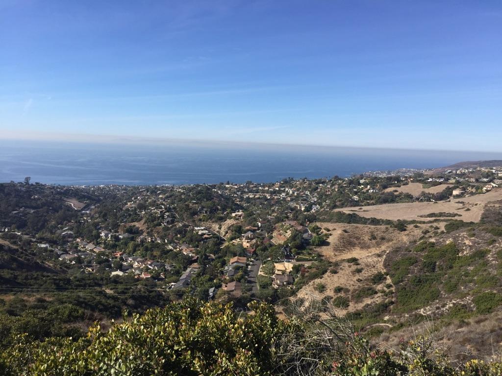 Panoramic view of a coastal town nestled in hills beside the vast ocean.
