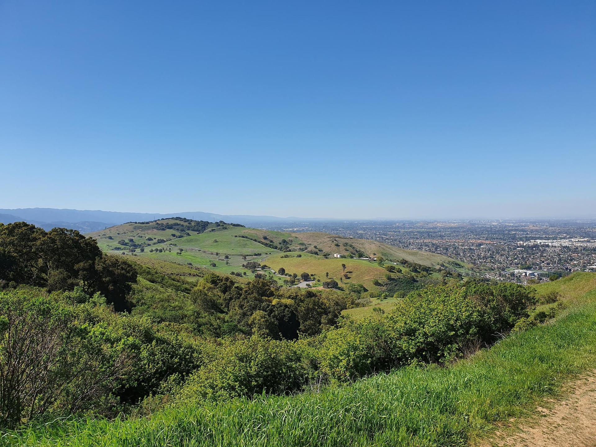 Vast green hills overlooking a distant city under a clear blue sky.