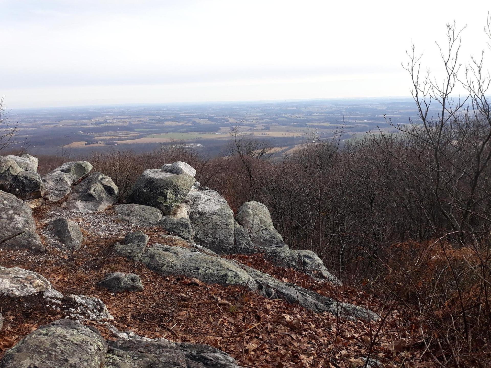 Rocky outcrop overlooks a vast, hazy valley under an overcast sky.