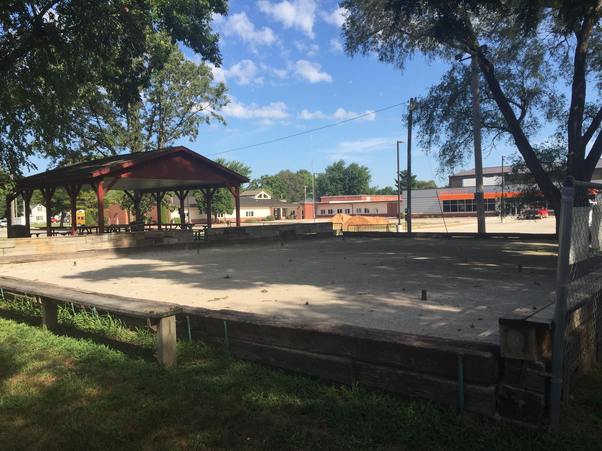 A large, empty sand court with a covered pavilion under a bright sky.