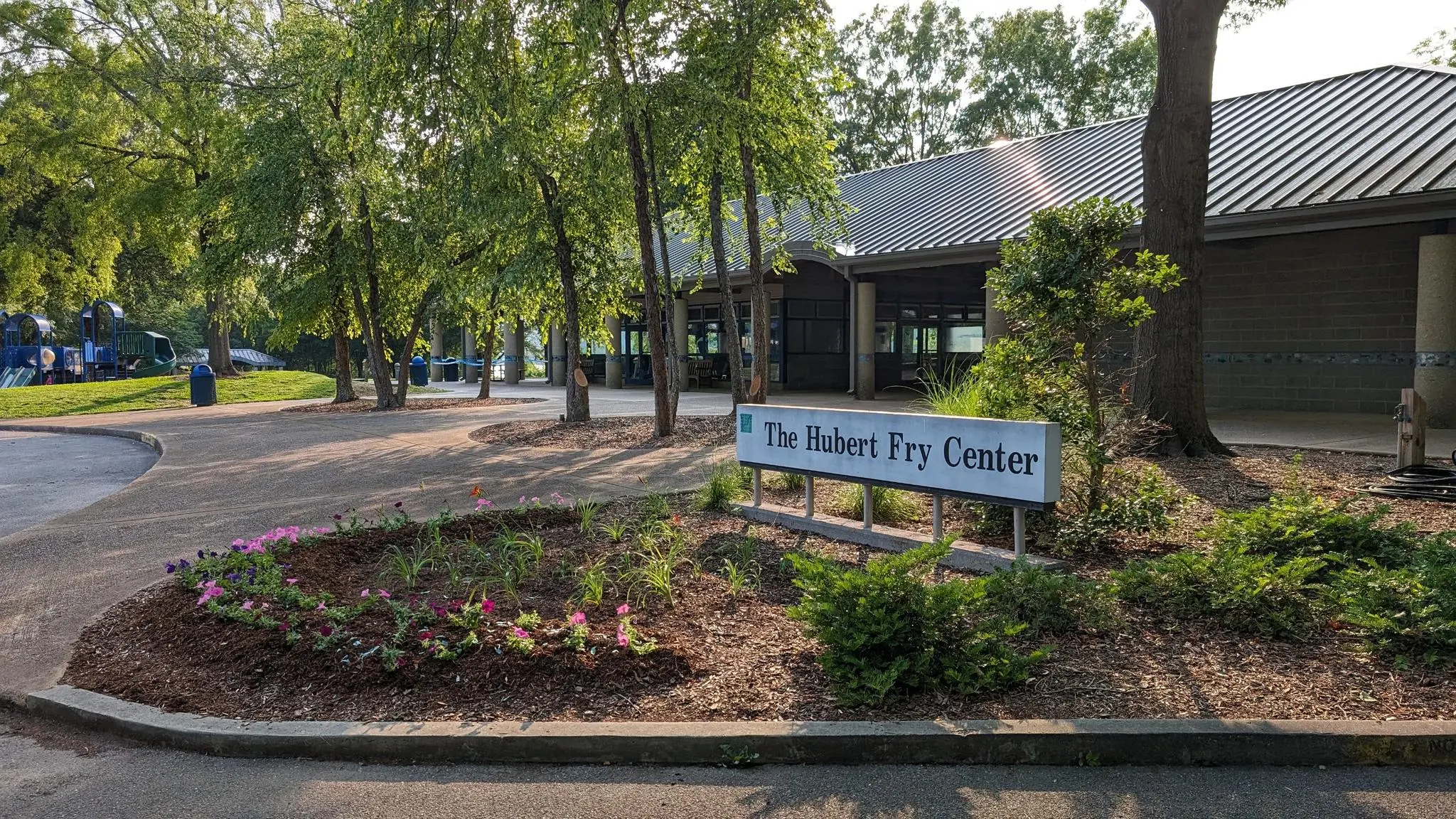 A building entrance with a sign, surrounded by trees and a paved area.