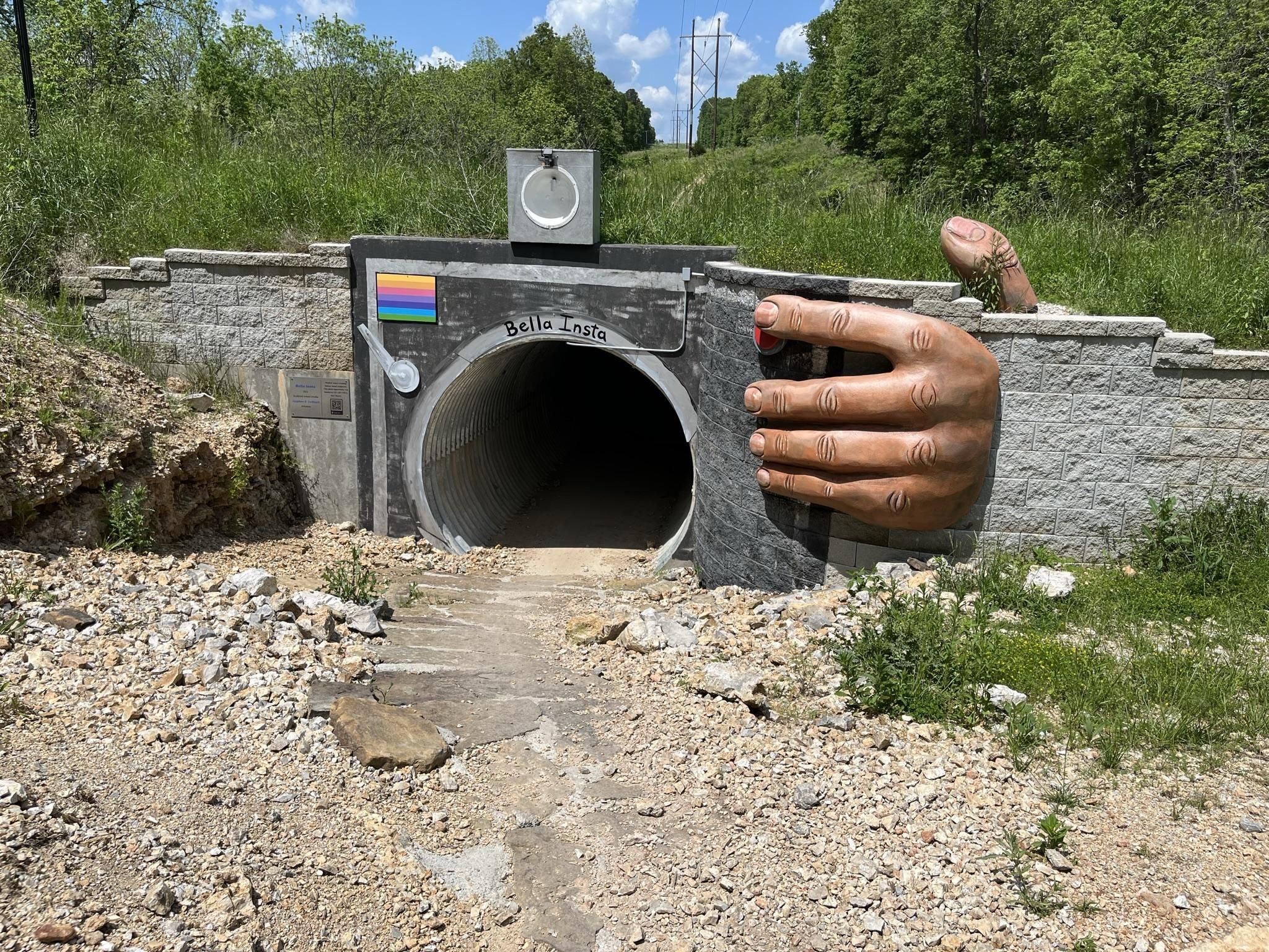 A tunnel entrance with a large hand mural and rainbow flag on a sunny day. - Tweety Bird Trail