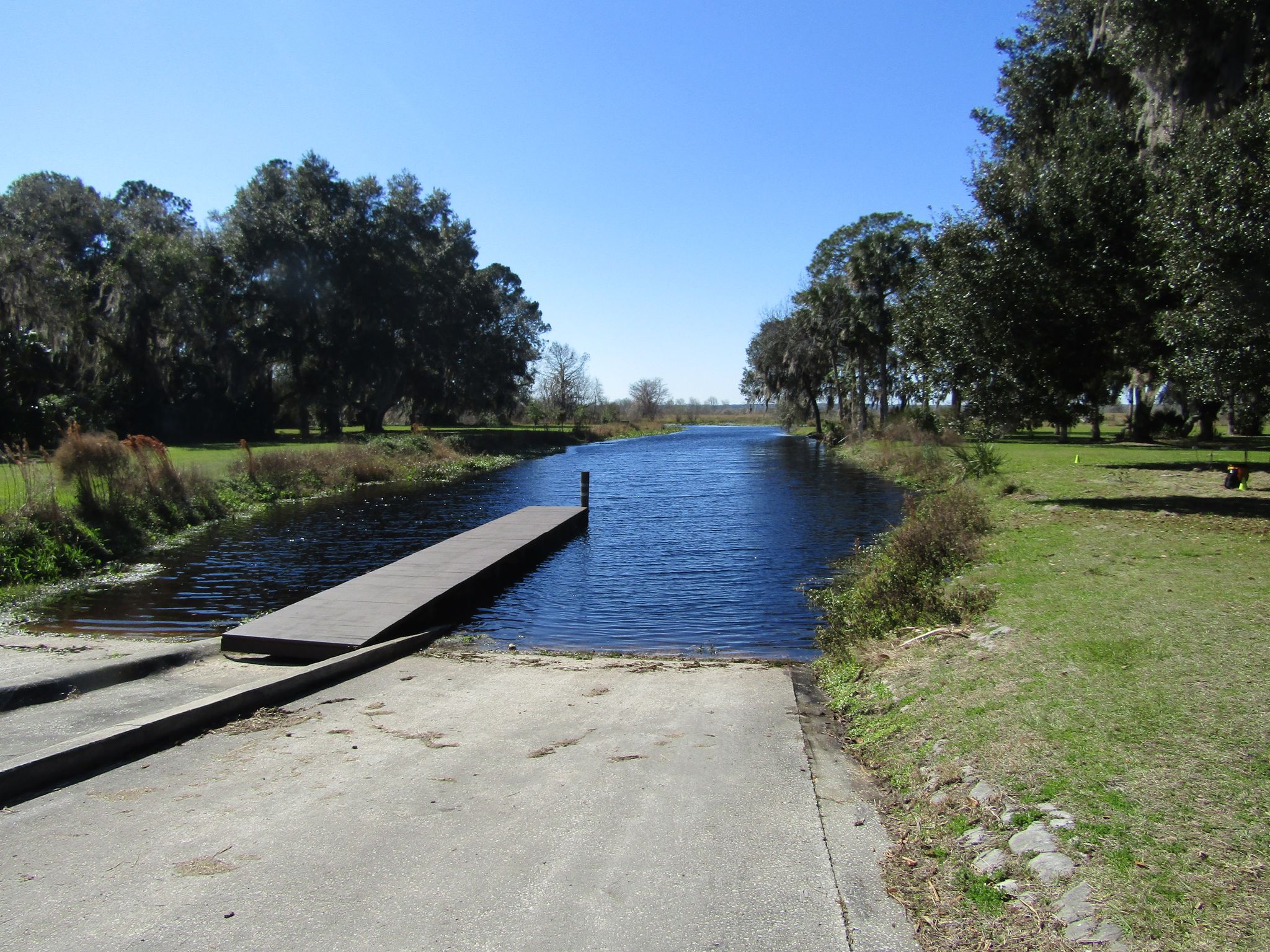 Concrete boat ramp leading into a calm, narrow waterway on a sunny day. - Orange Lake loop from Reddick, Florida