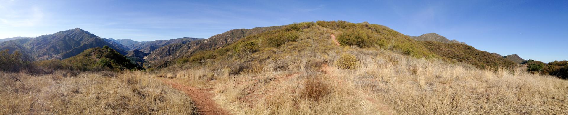 Panoramic view of a dirt trail winding through dry grassy hills.