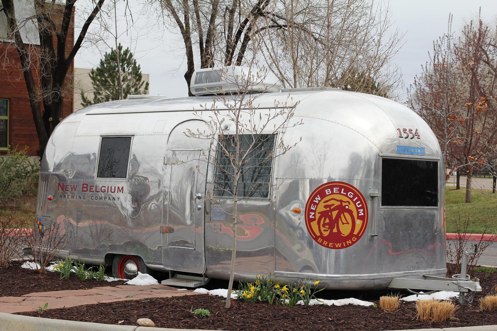 Shiny silver trailer with a red logo parked on mulched ground with bare trees.