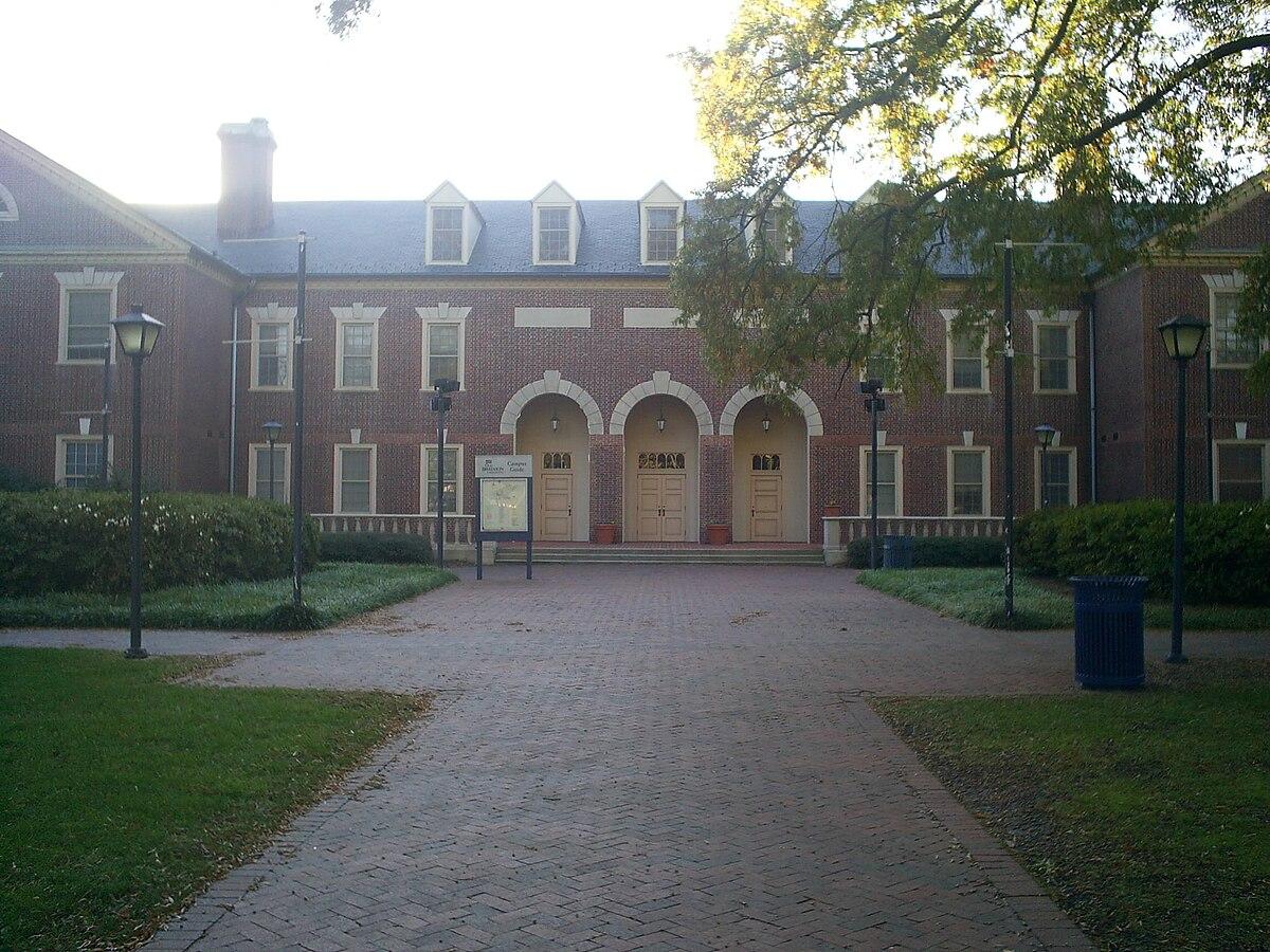 Brick building with arched entrances and a paved walkway on a sunny day.