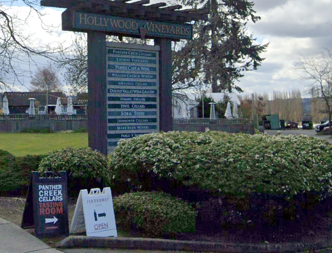 A large wooden sign for vineyards and wineries, surrounded by green bushes.