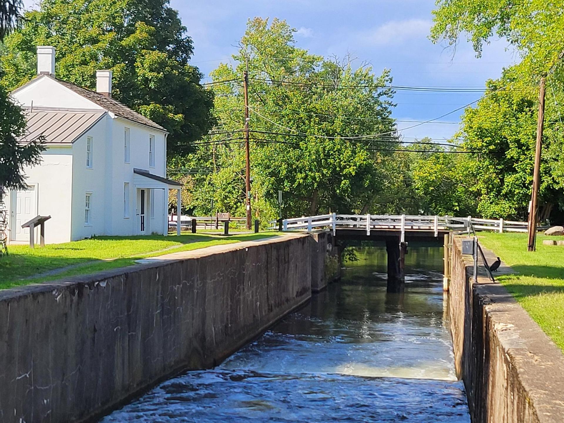 A white house next to a flowing canal with a small white bridge.