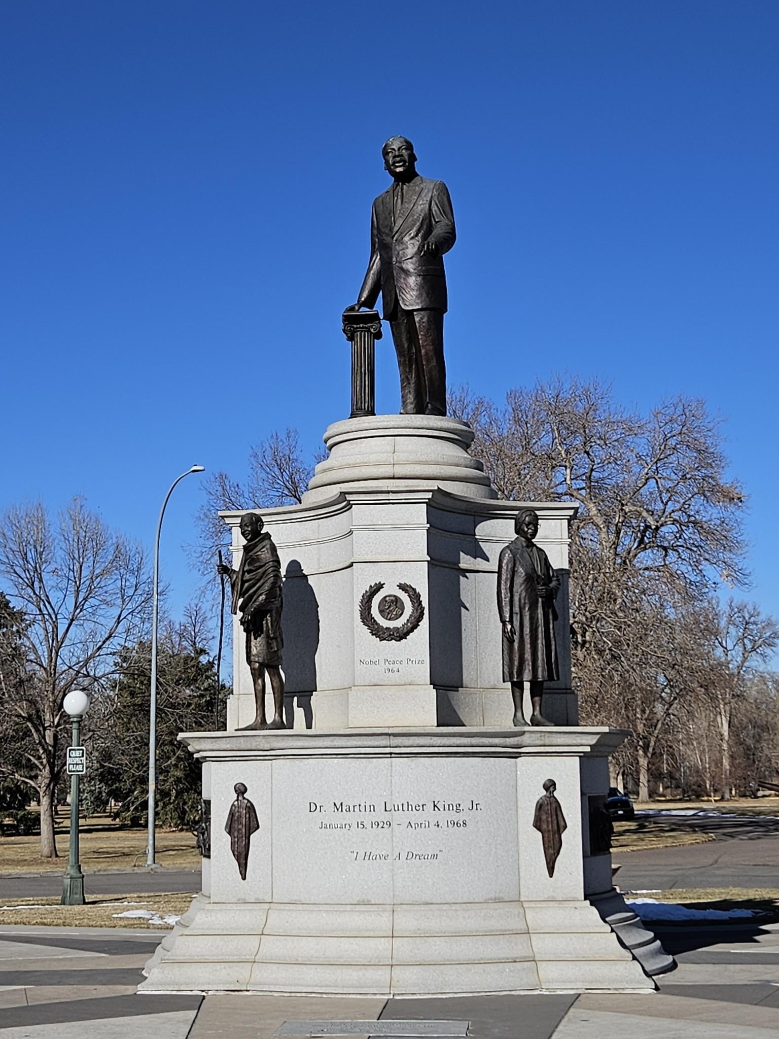 A tall bronze statue on a multi-tiered stone pedestal under a clear blue sky.