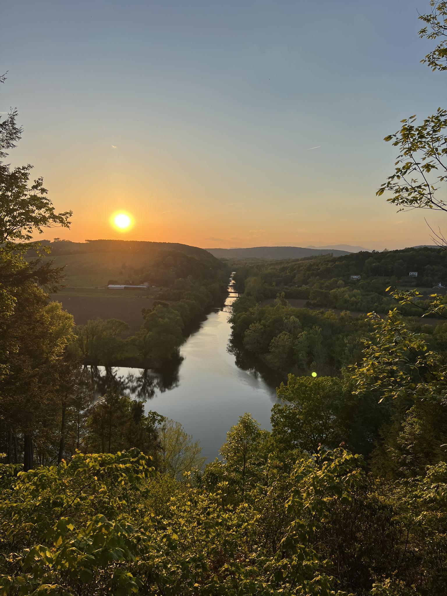 Golden sunset over a winding river surrounded by lush green trees.