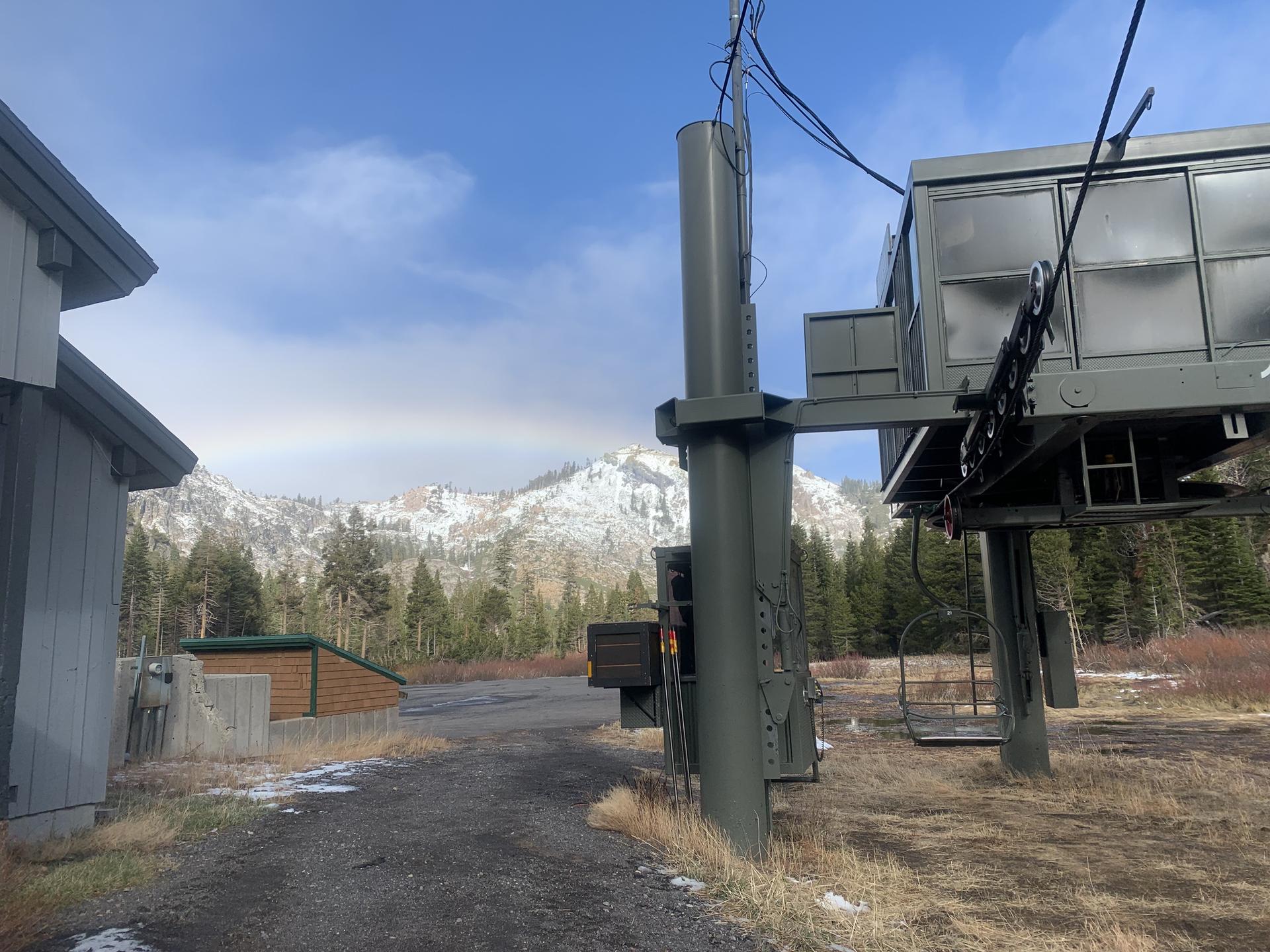 Ski lift base with snowy mountains and evergreen trees under a bright sky.