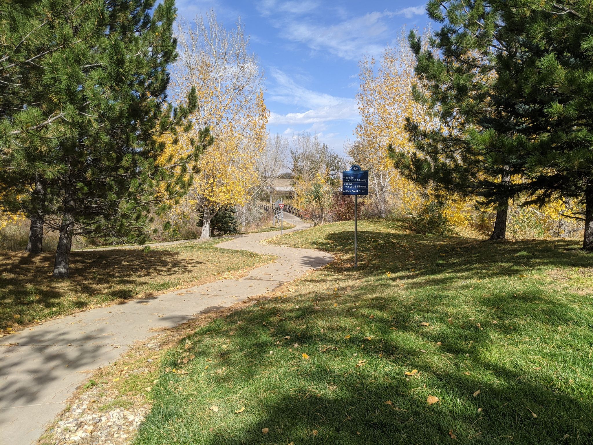 Paved path winding through a sunny park with green and yellow autumn trees. - Frank Varra Park Loop