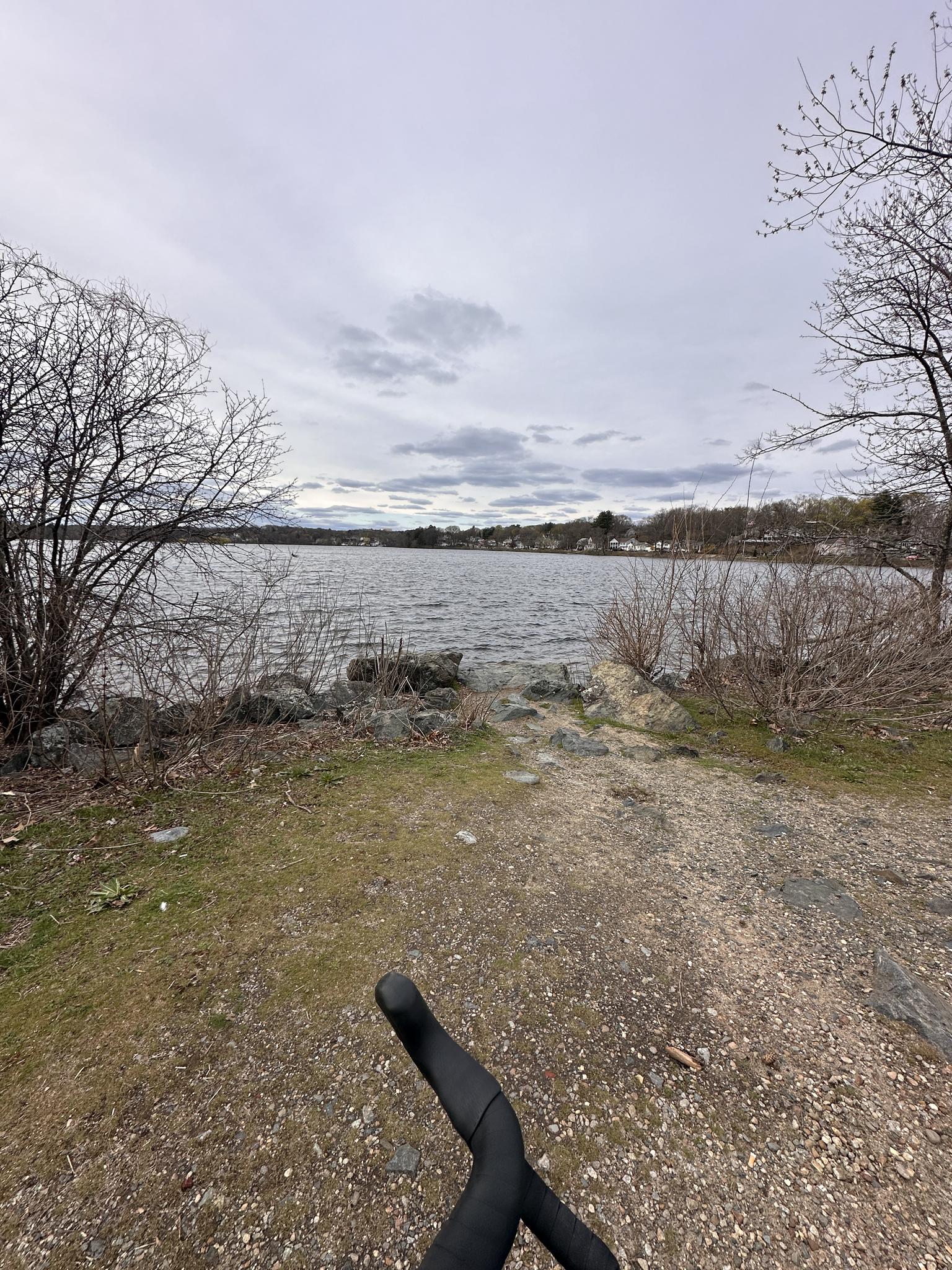 Bicycle handlebars on a dirt path overlooking a wide lake.