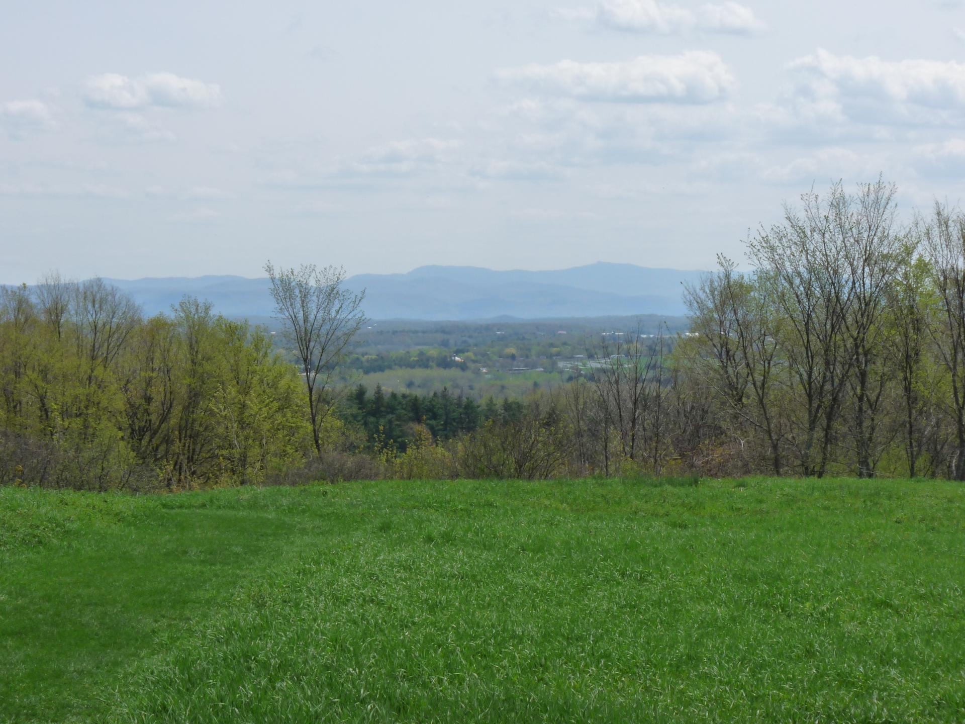 Green field overlooking a valley with distant hazy mountains and trees.