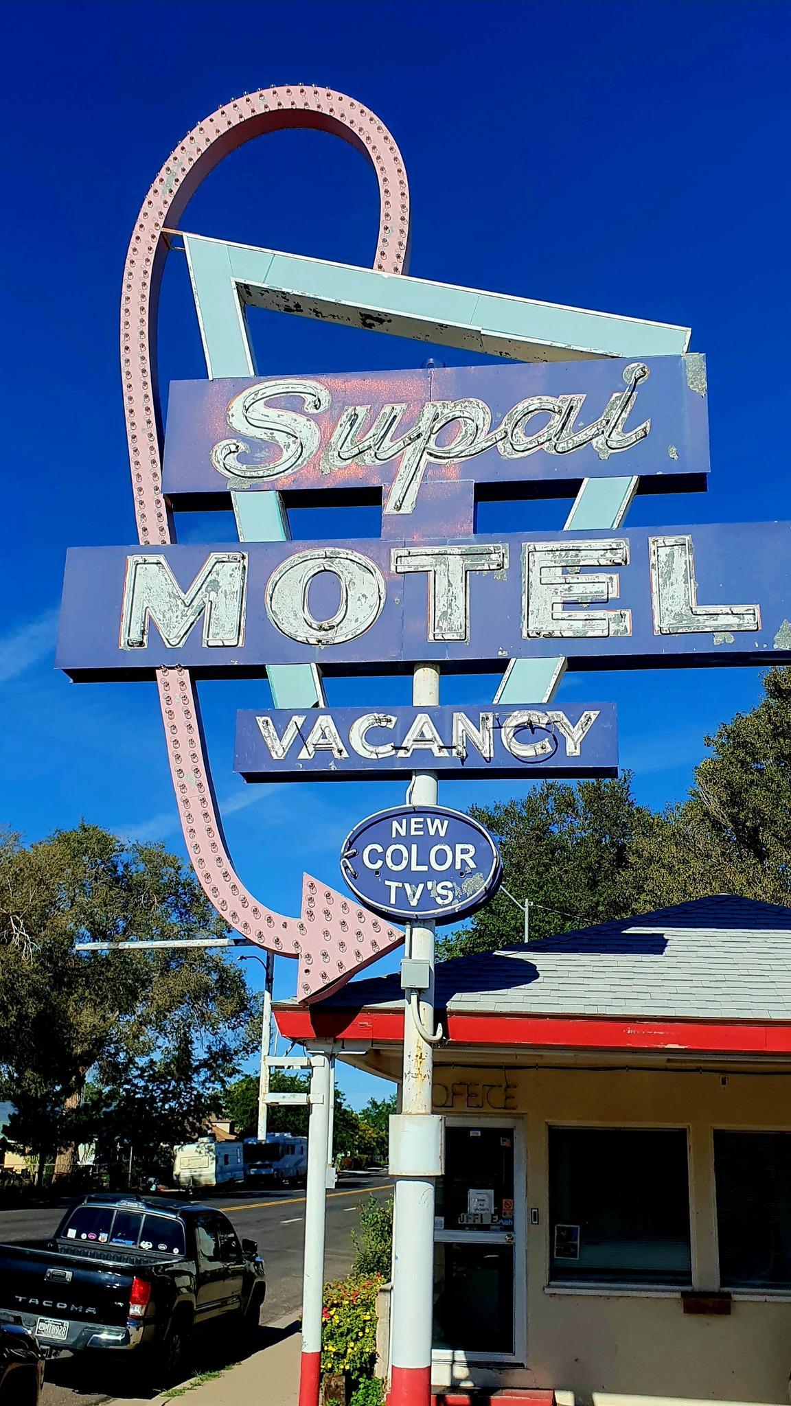 Vintage "Supai Motel" sign with "Vacancy" and "New Color TV's" under blue sky.