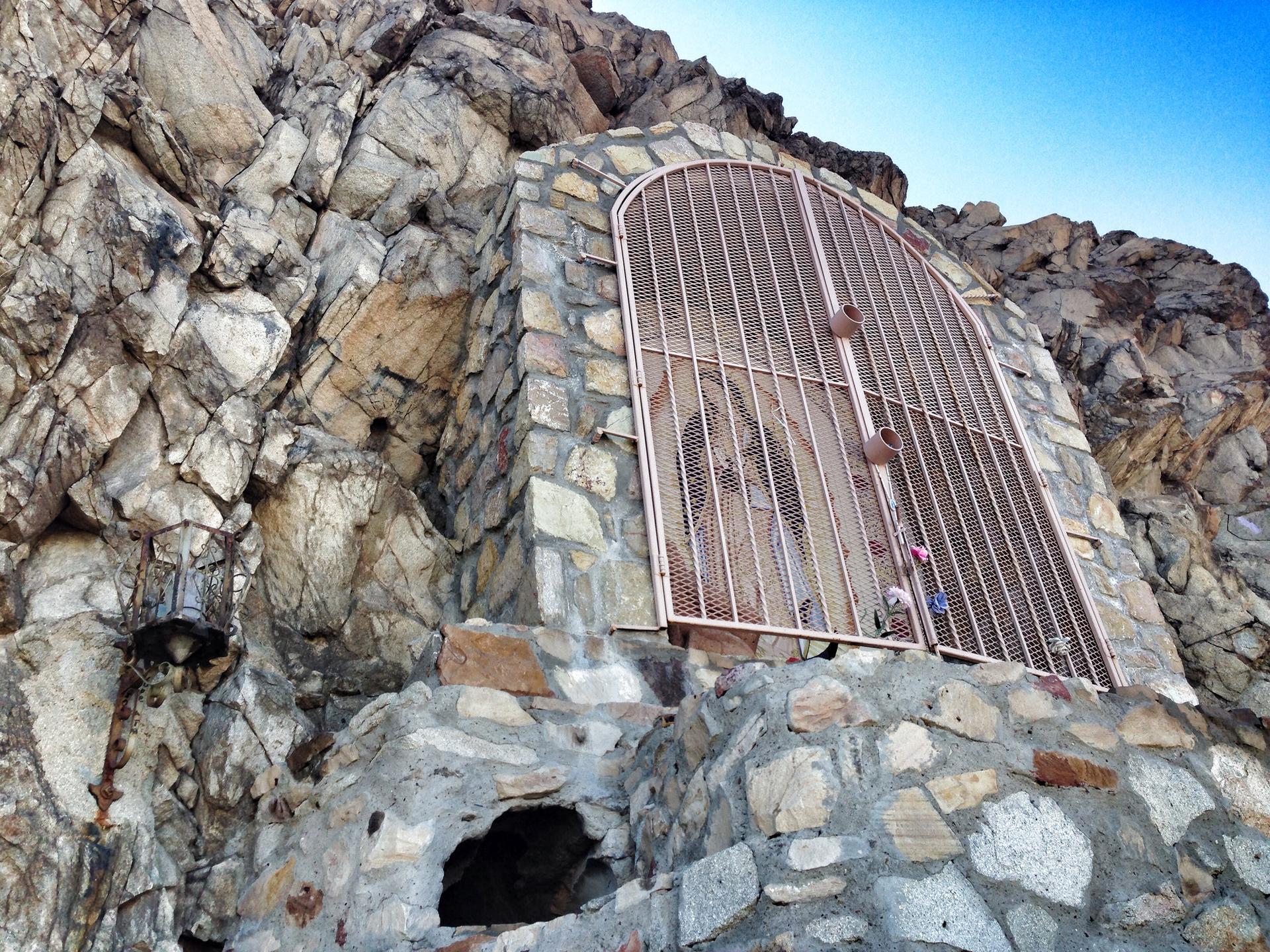 Stone grotto with a metal gate built into a rocky cliff face.