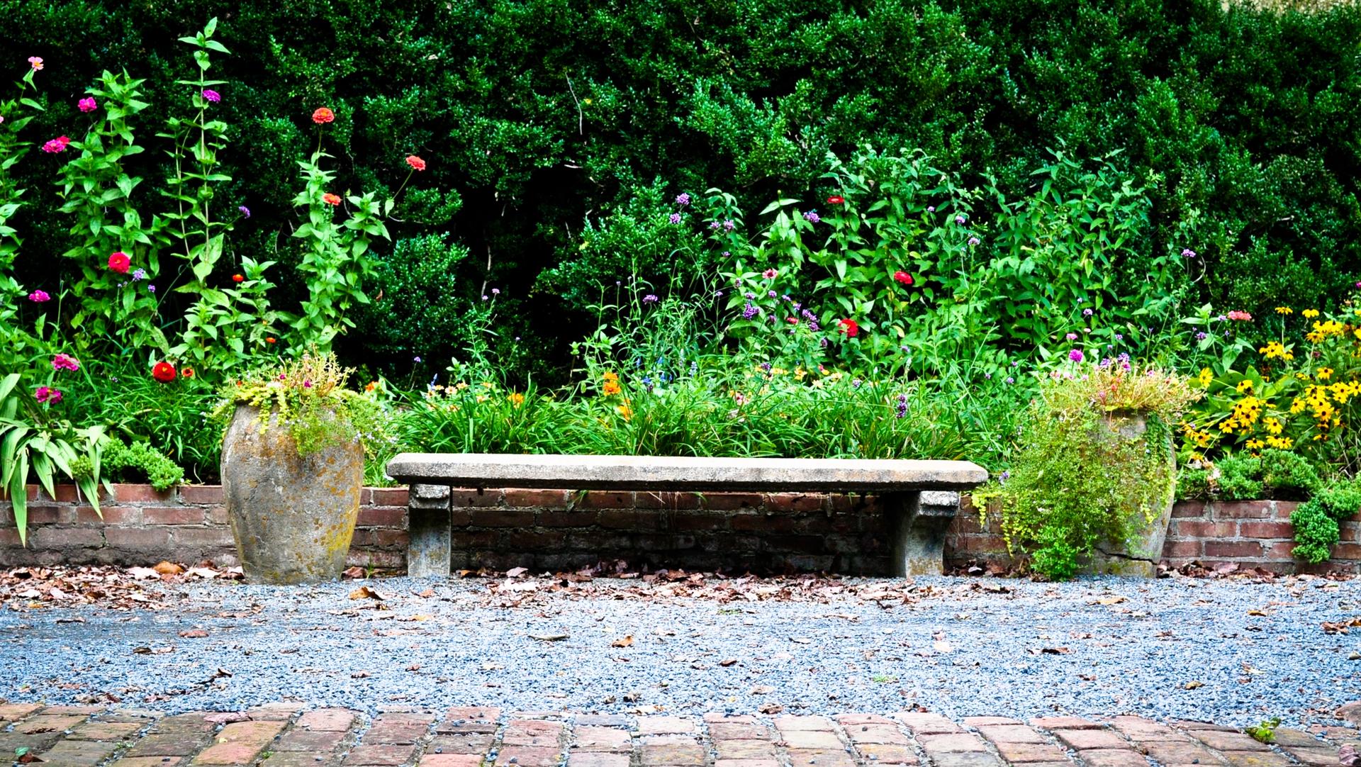 A garden bench between two large planters with vibrant green foliage and flowers.