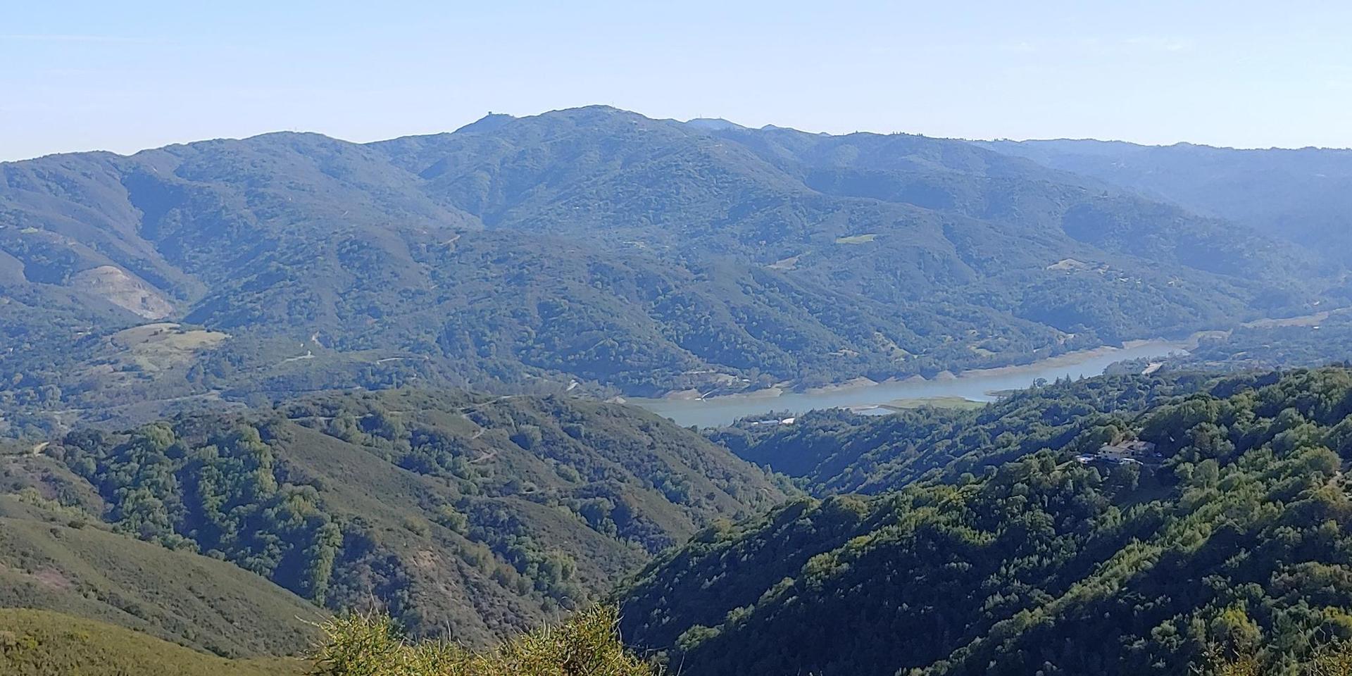 Panoramic view of green, rolling mountains and a valley with a distant body of water.