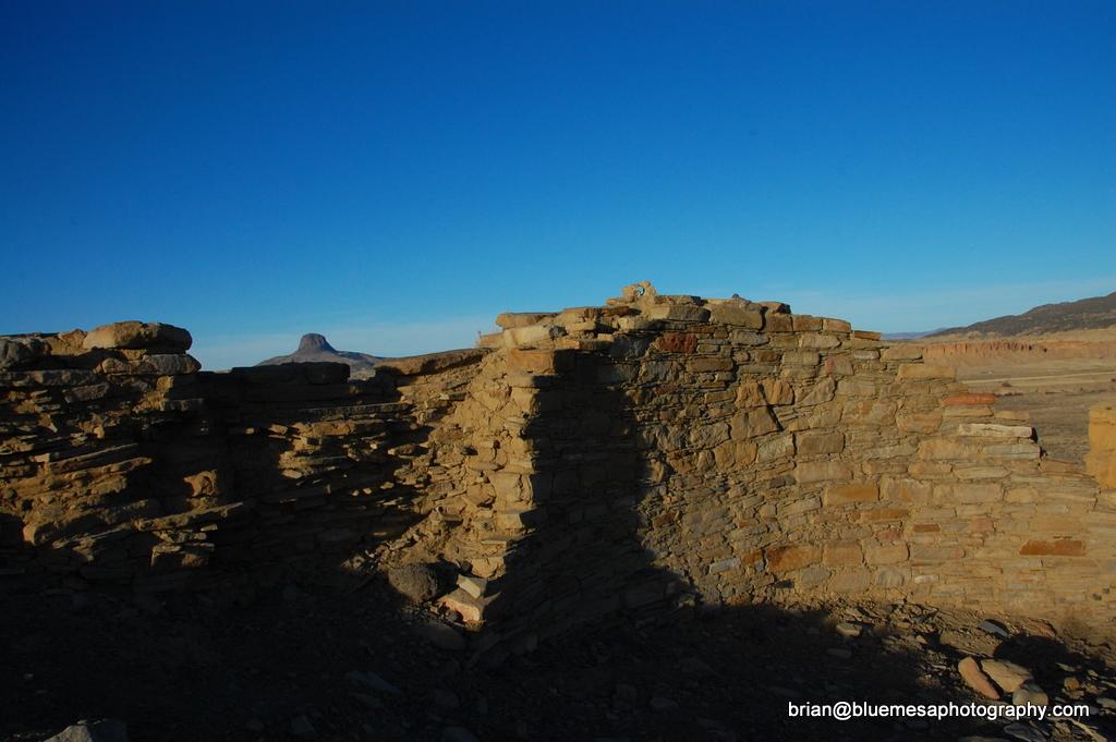 Sunlit ancient stone ruins with long shadows under a clear blue sky.