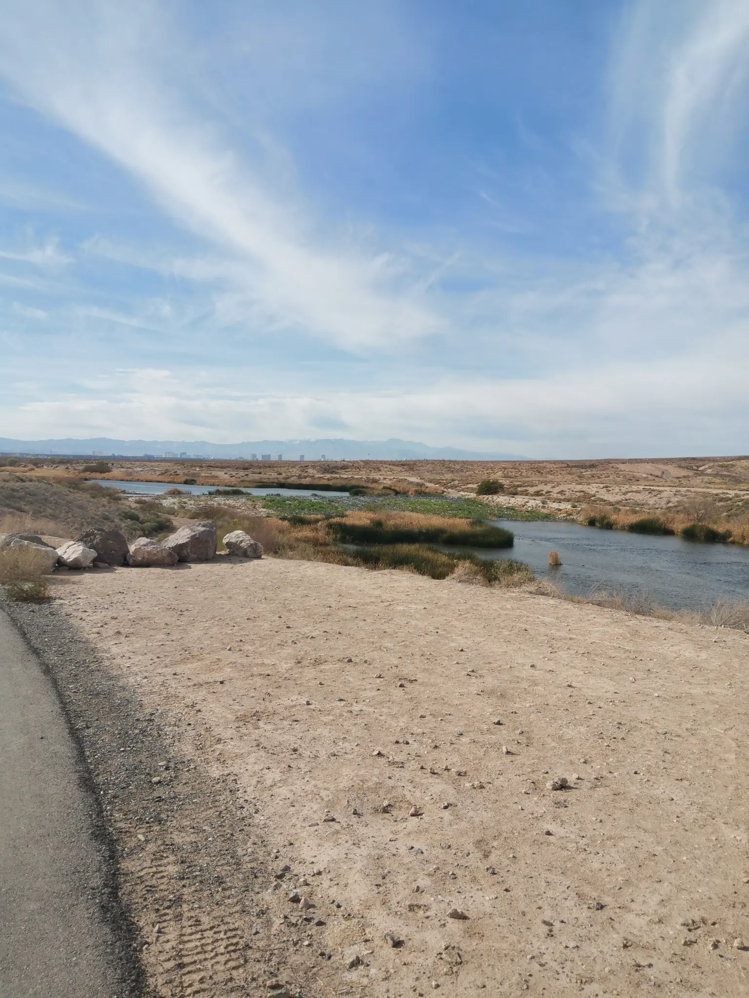 A river flows through a dry, reedy landscape under a bright blue sky.