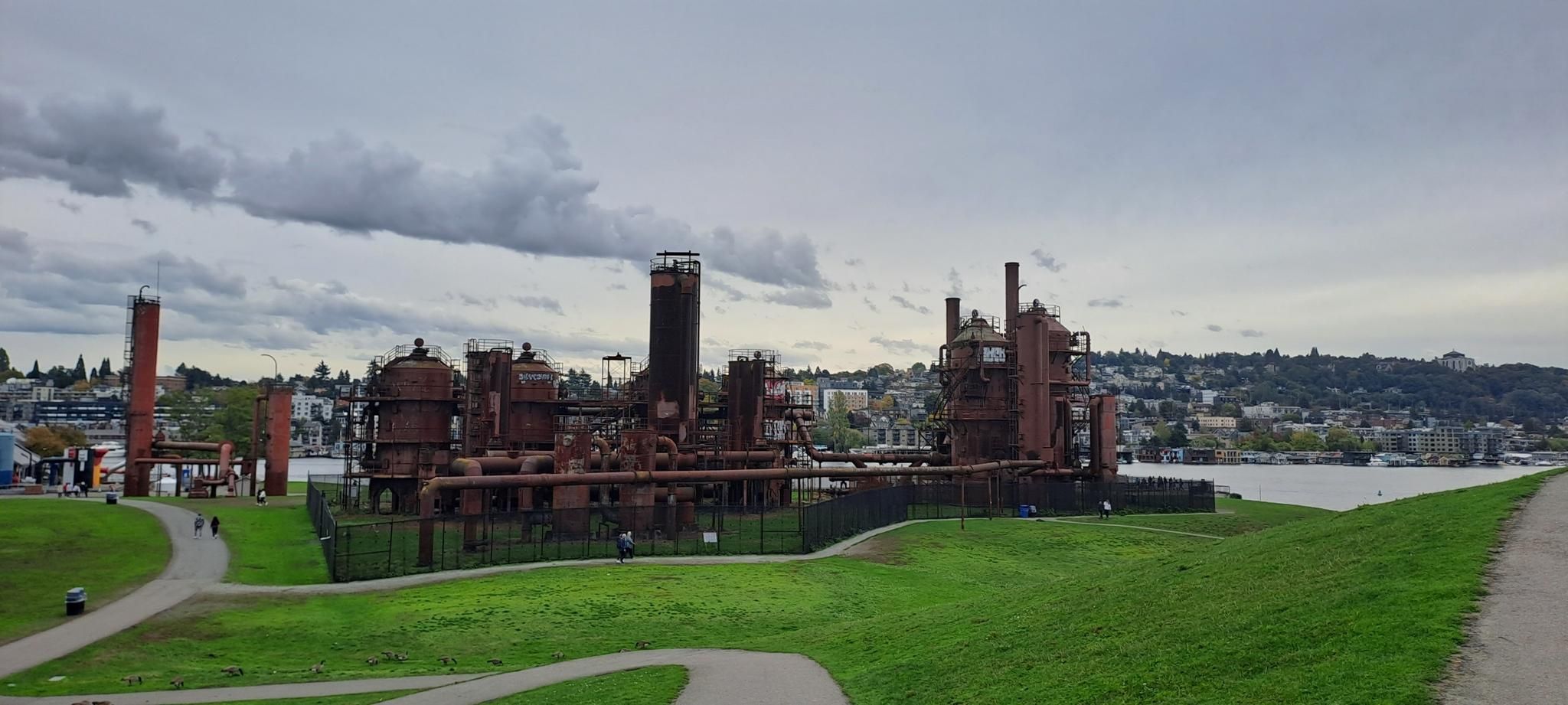 Rusty industrial structures on a green hill by water under an overcast sky. - Seattle: Lake Washington & Alki Trail Loop