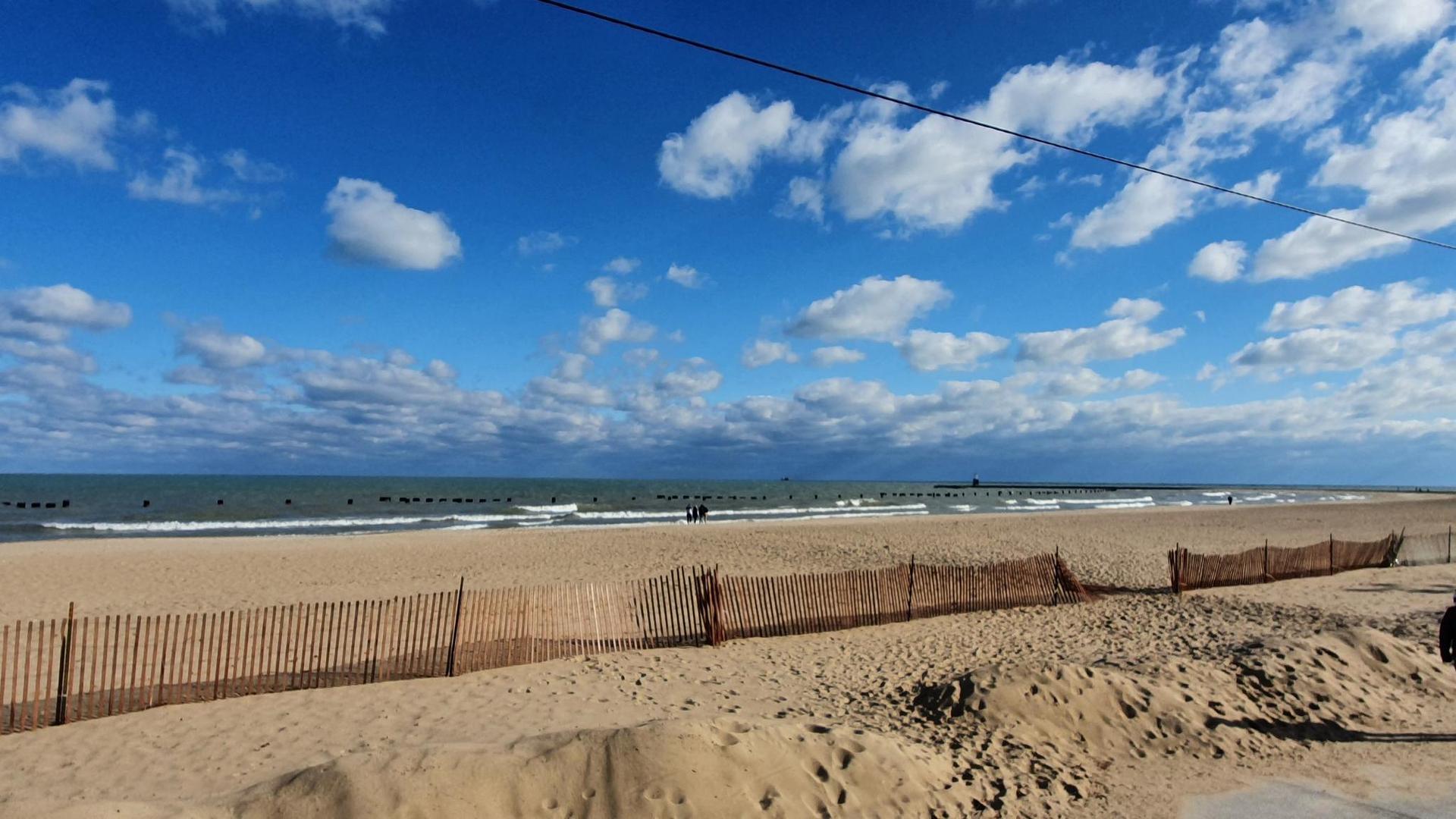 A sandy beach with a wooden fence, ocean waves, and a bright blue sky.