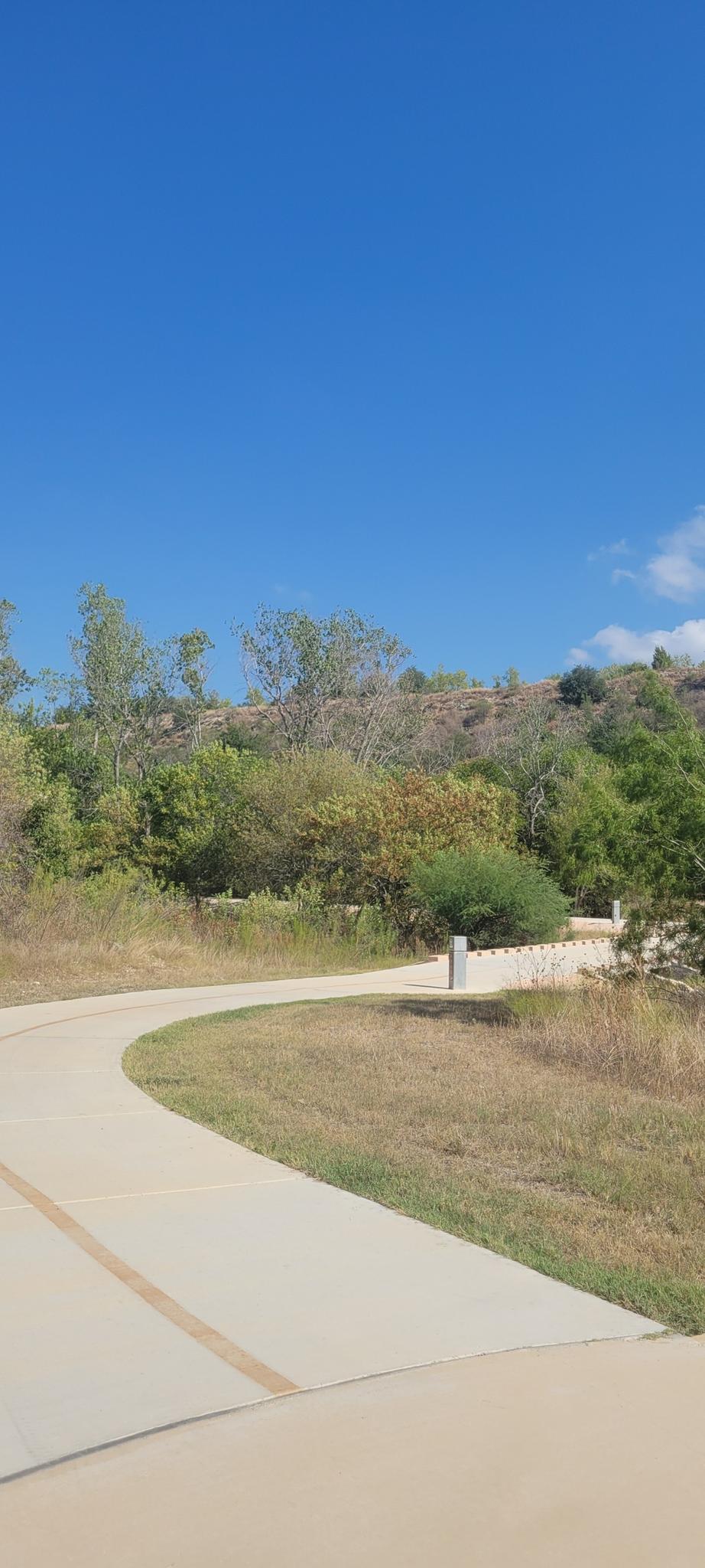 A winding paved path leads through grassy hills under a clear blue sky.