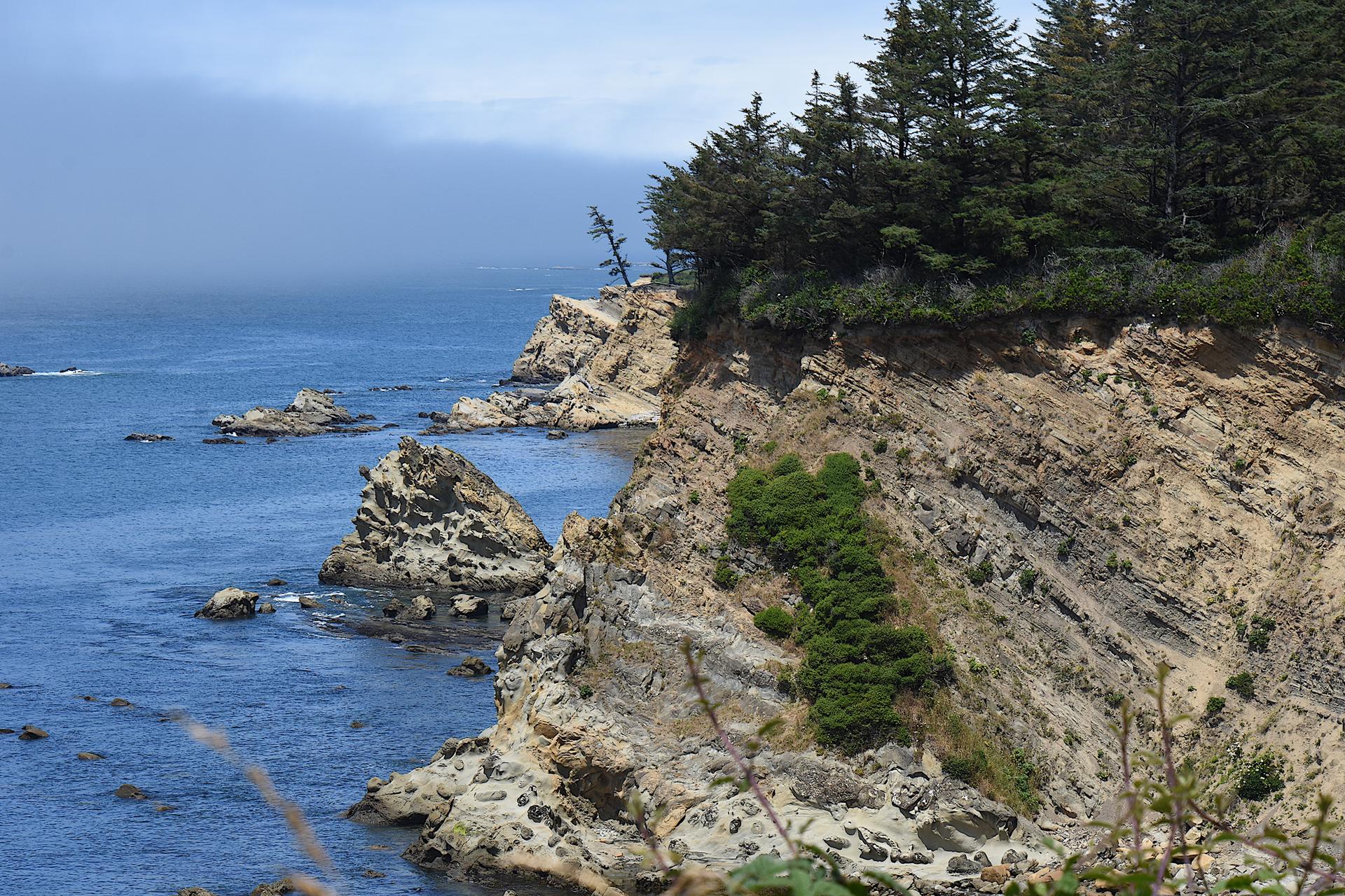 Sunny view of rugged coastal cliffs, deep blue ocean, and scattered sea stacks.