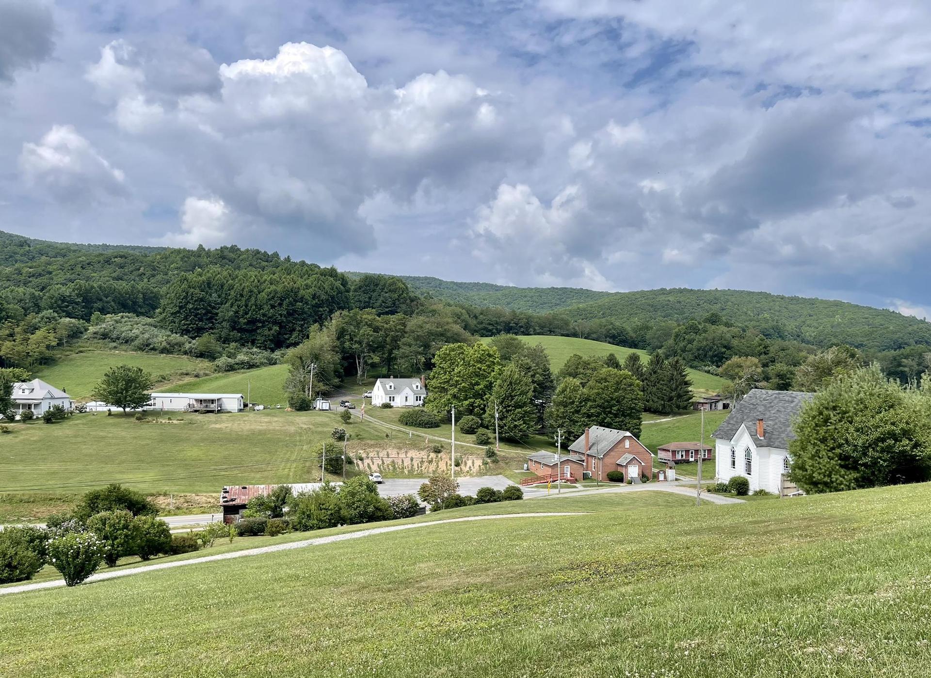 Village nestled in green rolling hills under a cloudy sky.