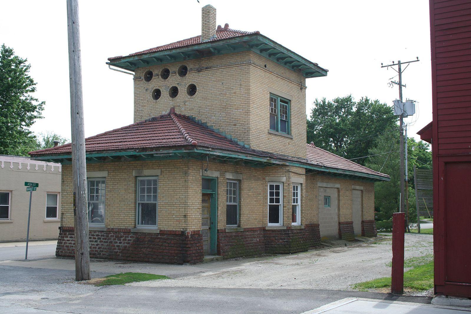 An old brick building with a central tower and red roof on an overcast day.