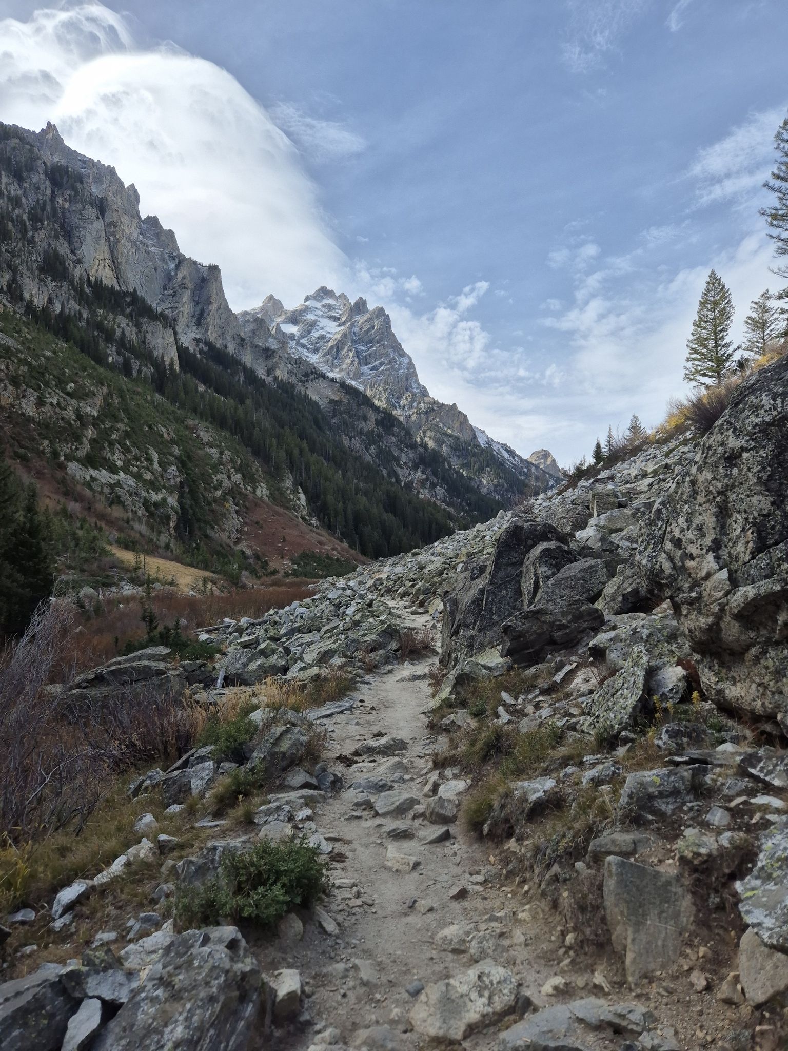 A rocky trail winds through a mountain valley with steep slopes and distant peaks. - Teton Crest Trail: Granite Canyon to Jenny Lake