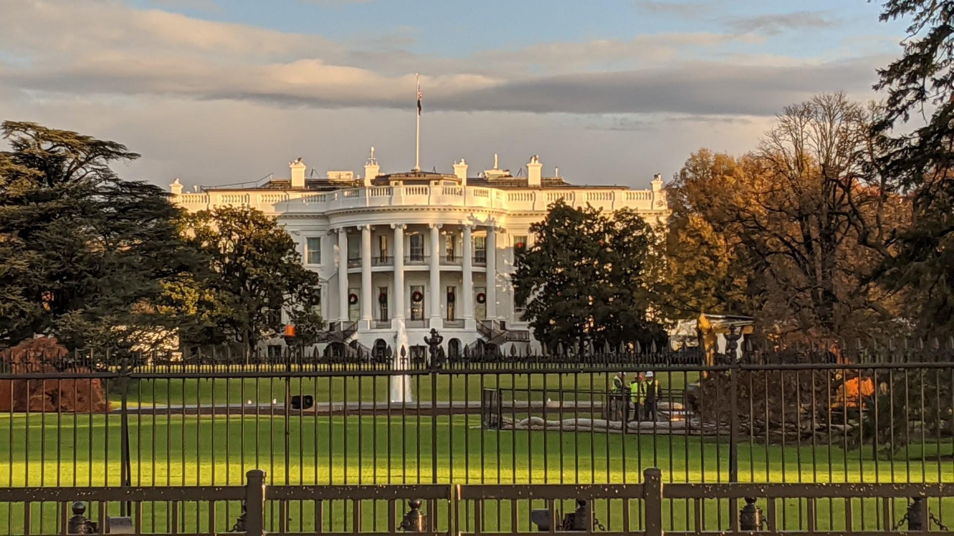 Grand white building with columns behind a fence, under a cloudy sky.