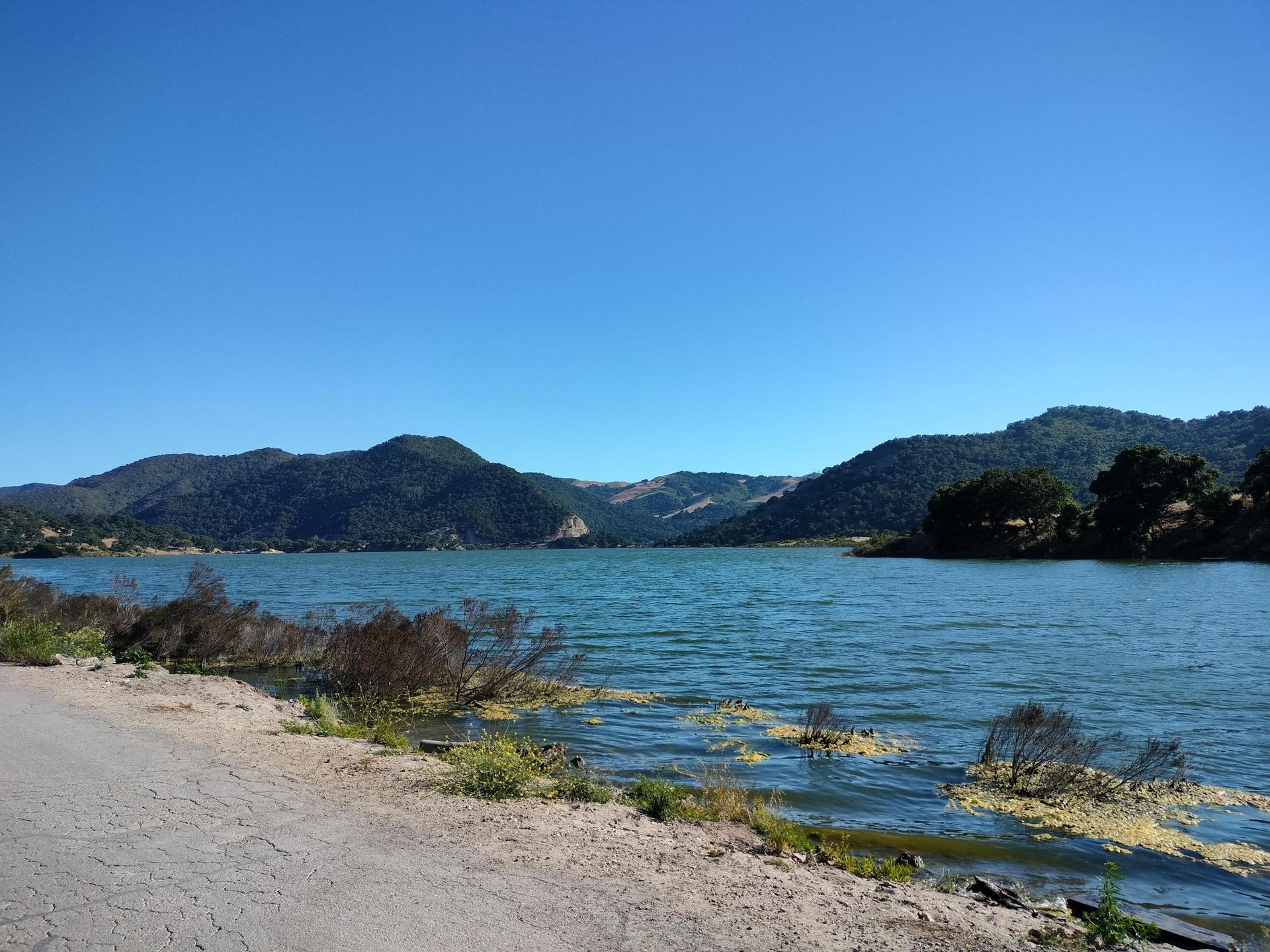 Wide blue lake with green hills in the background under a clear sky.
