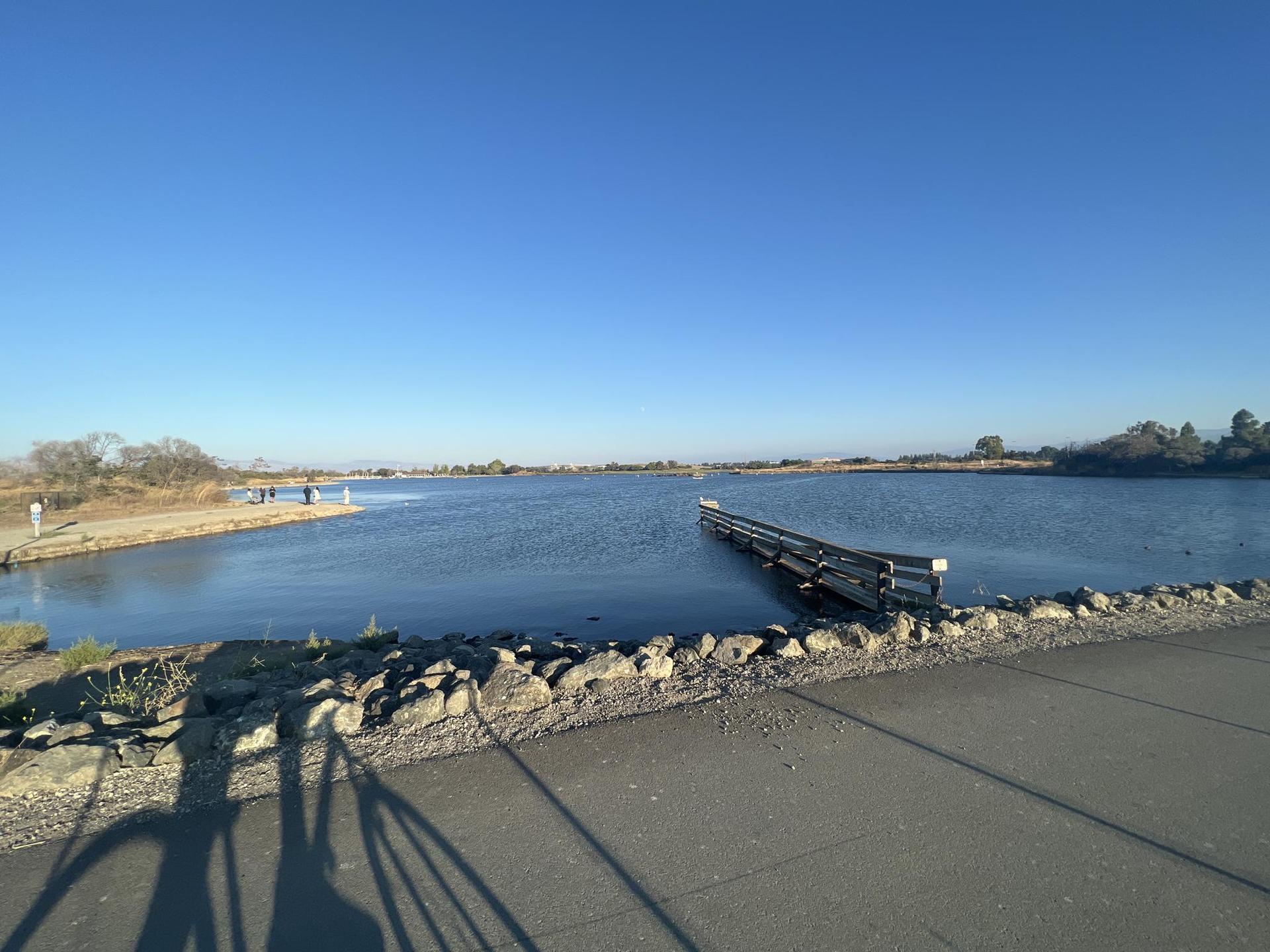 A wide body of water with a partially submerged dock under a bright blue sky.