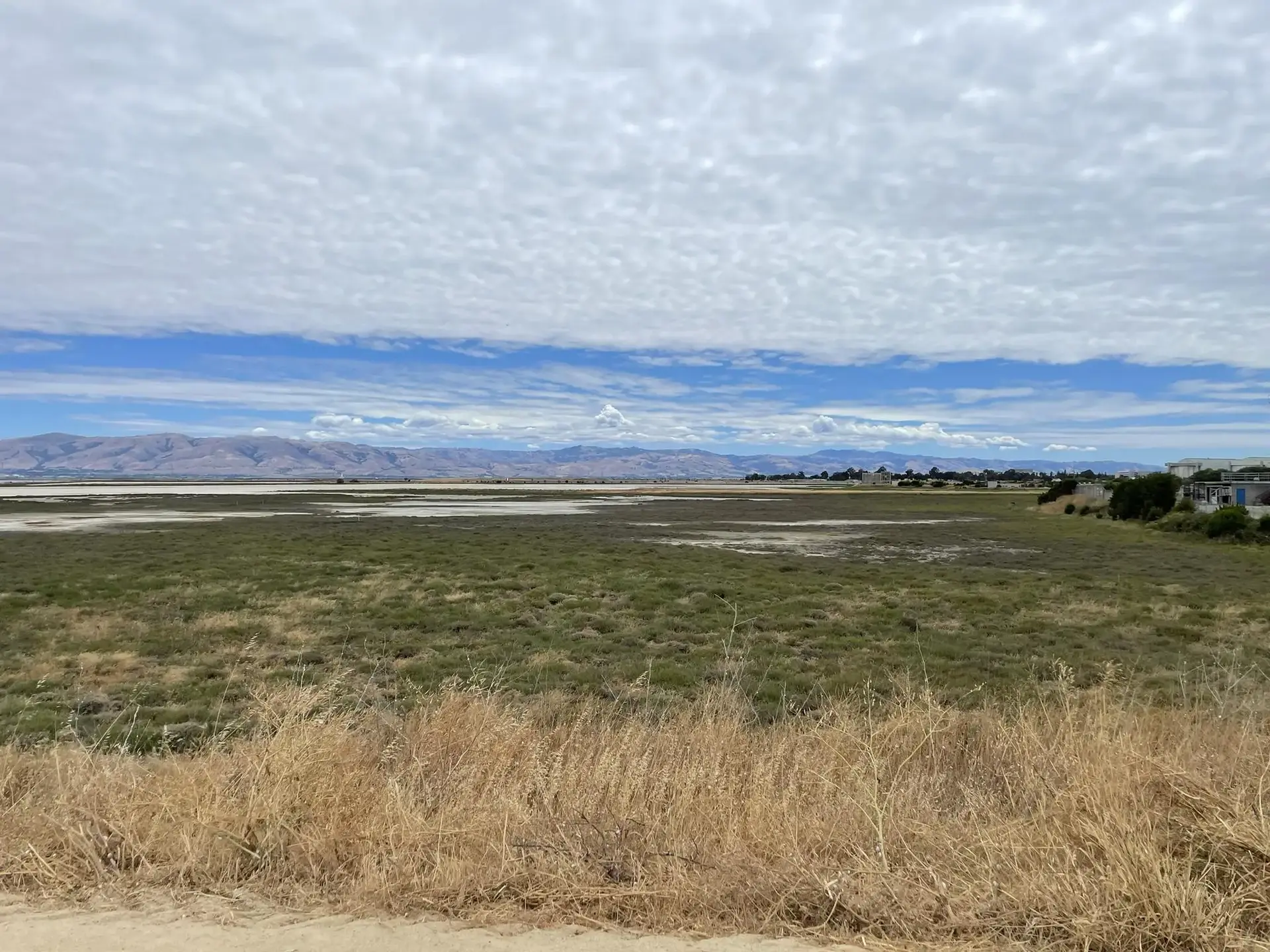 Vast green and dry fields stretch towards distant mountains under a cloudy sky.