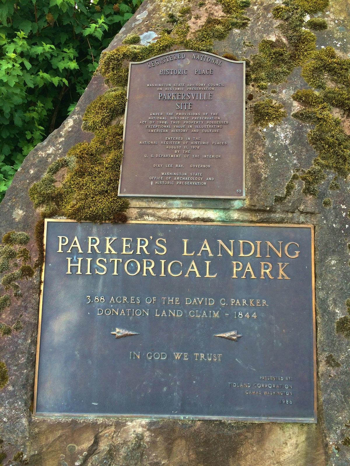 Two weathered bronze historical plaques on a moss-covered rock.