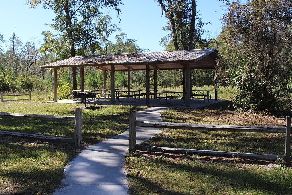 Sunny outdoor scene with a large wooden picnic pavilion and paved path.