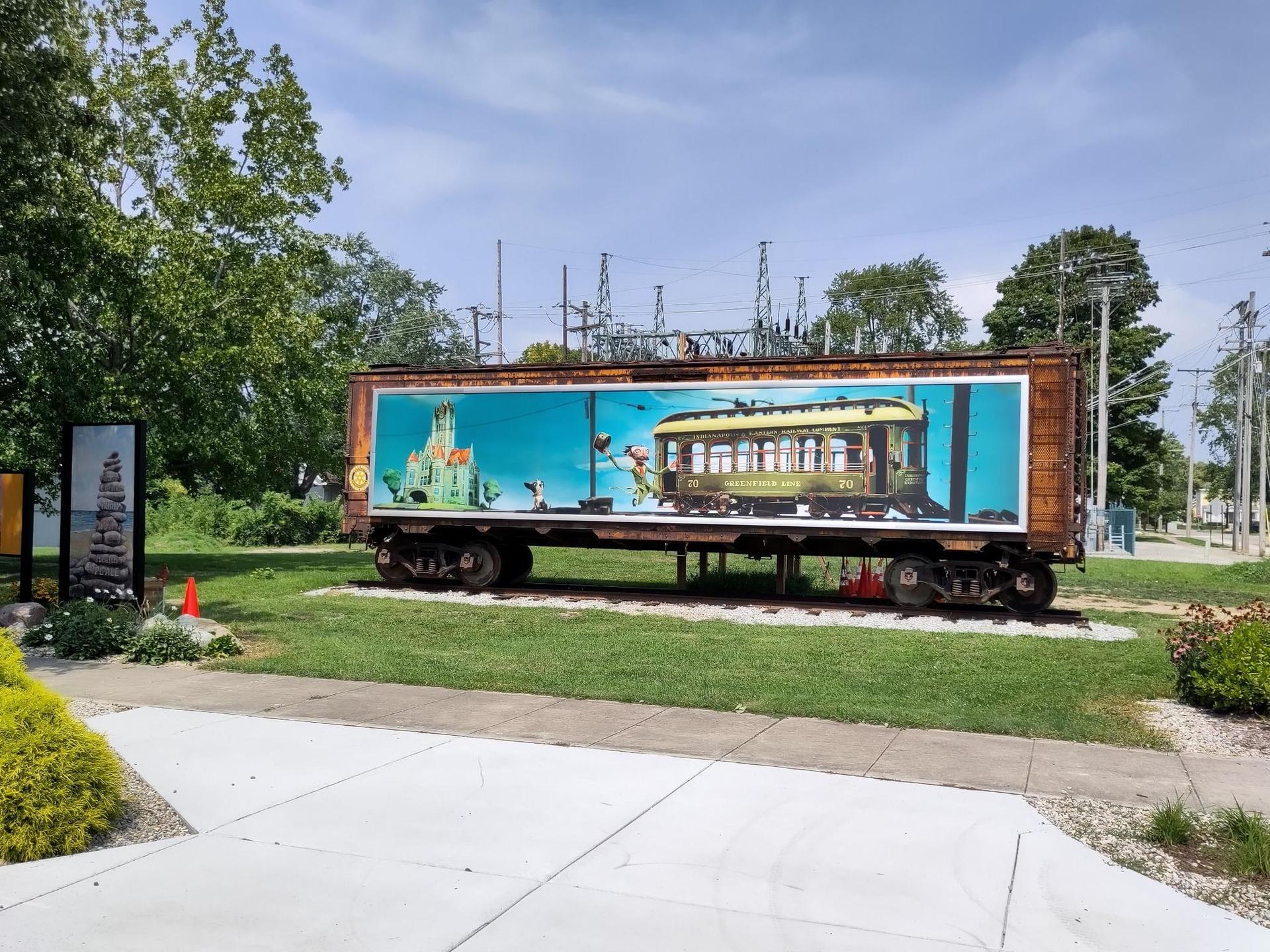 Old train car with a colorful mural on a grassy display area.