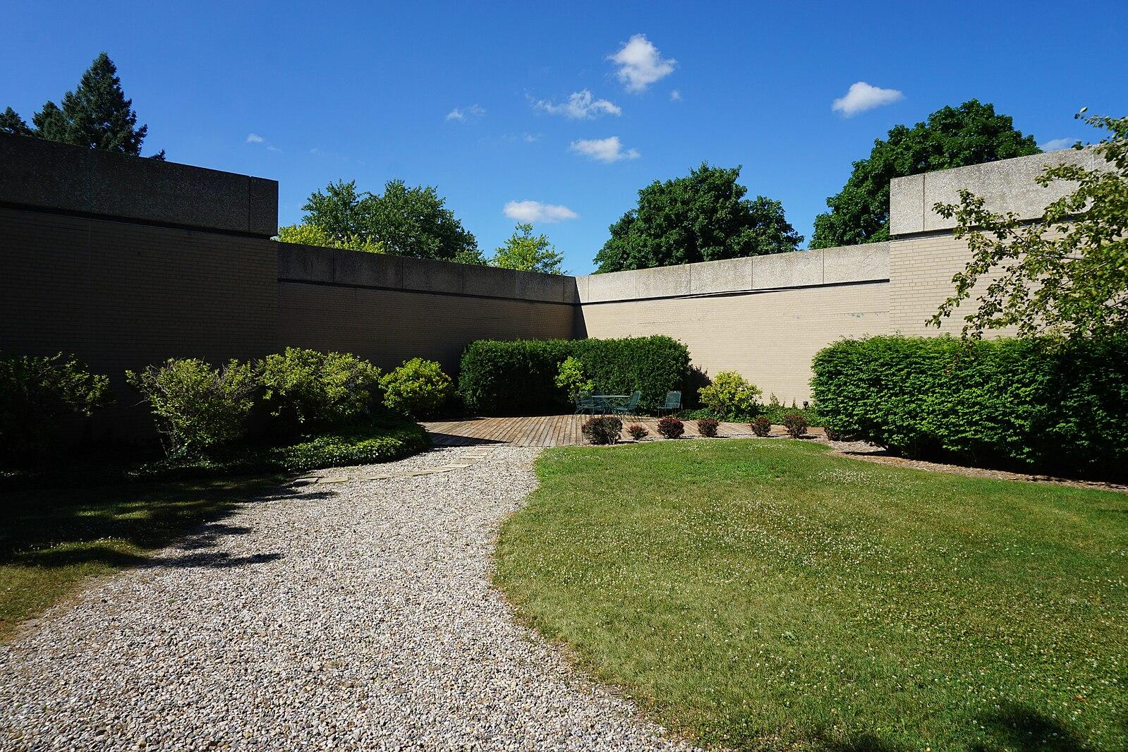 Gravel path, green lawn, concrete walls, and hedges under a bright blue sky.