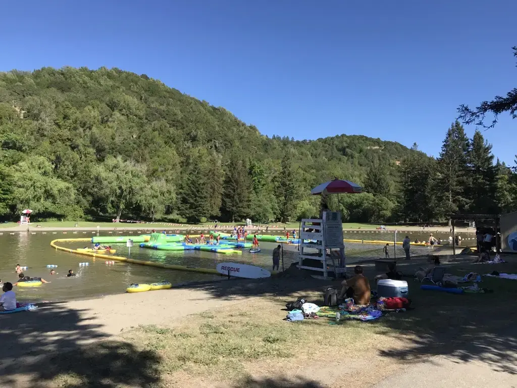 A lake with an inflatable obstacle course and many people swimming on a sunny day.