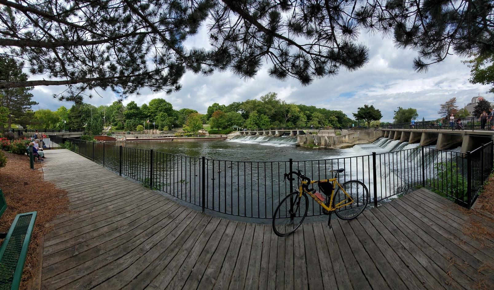 A river dam and waterfall next to a wooden boardwalk with a parked bicycle.