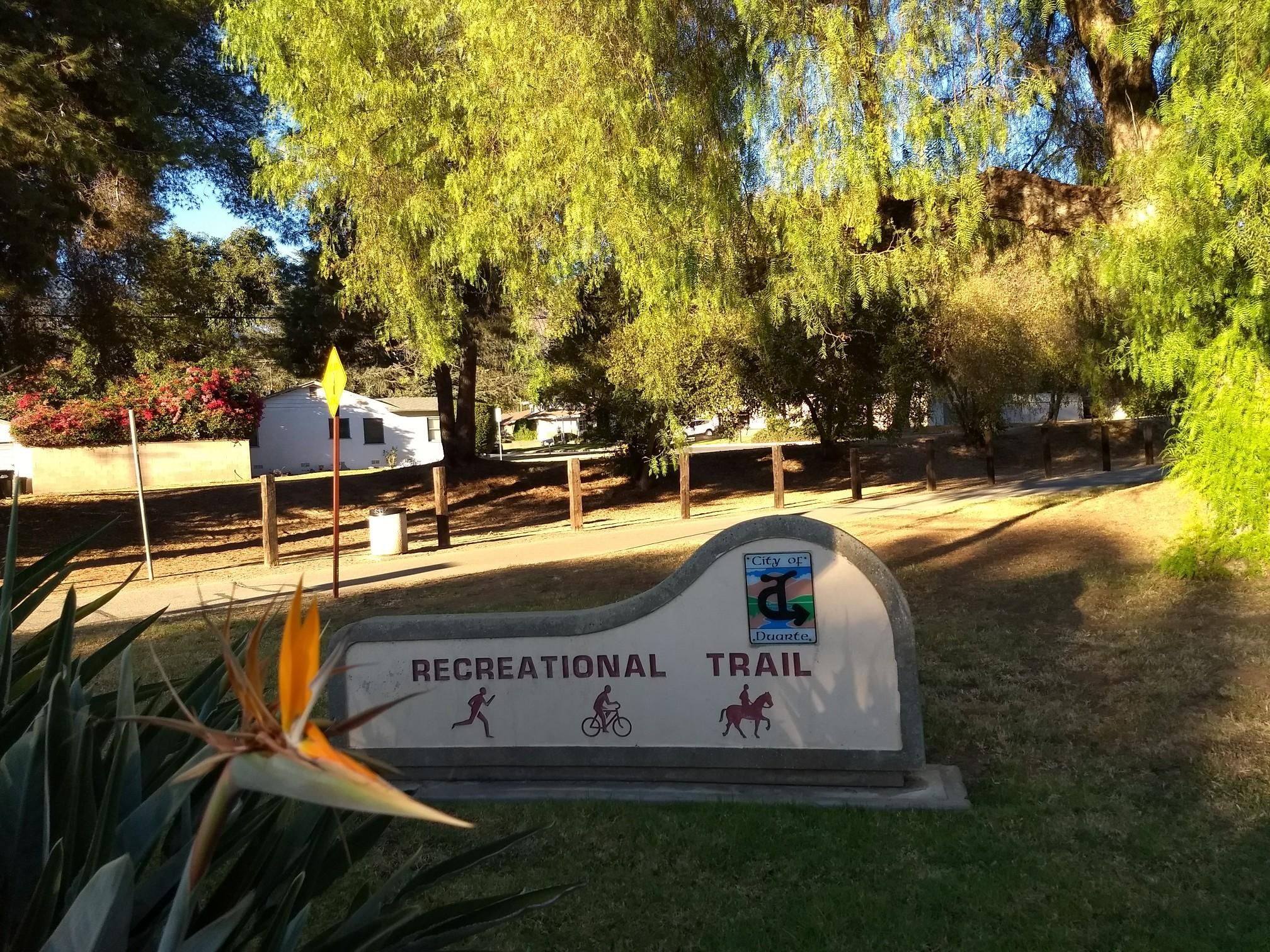 Recreational trail sign with a Bird of Paradise flower, bright sunlight, green trees. - Duarte Recreational Trail