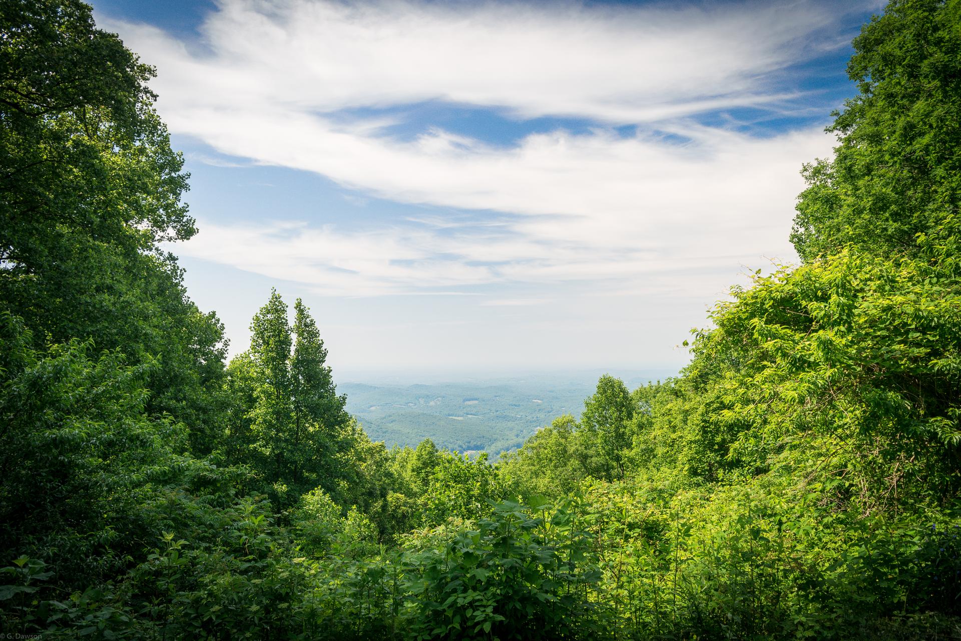 Lush green mountain valley under a bright, partly cloudy sky.