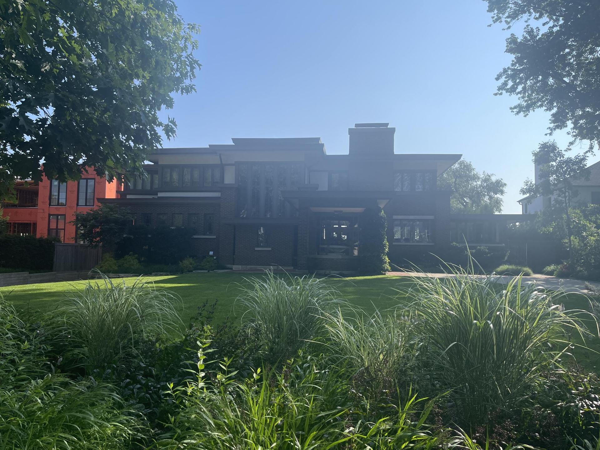Large modern house behind a green lawn and trees on a sunny day.