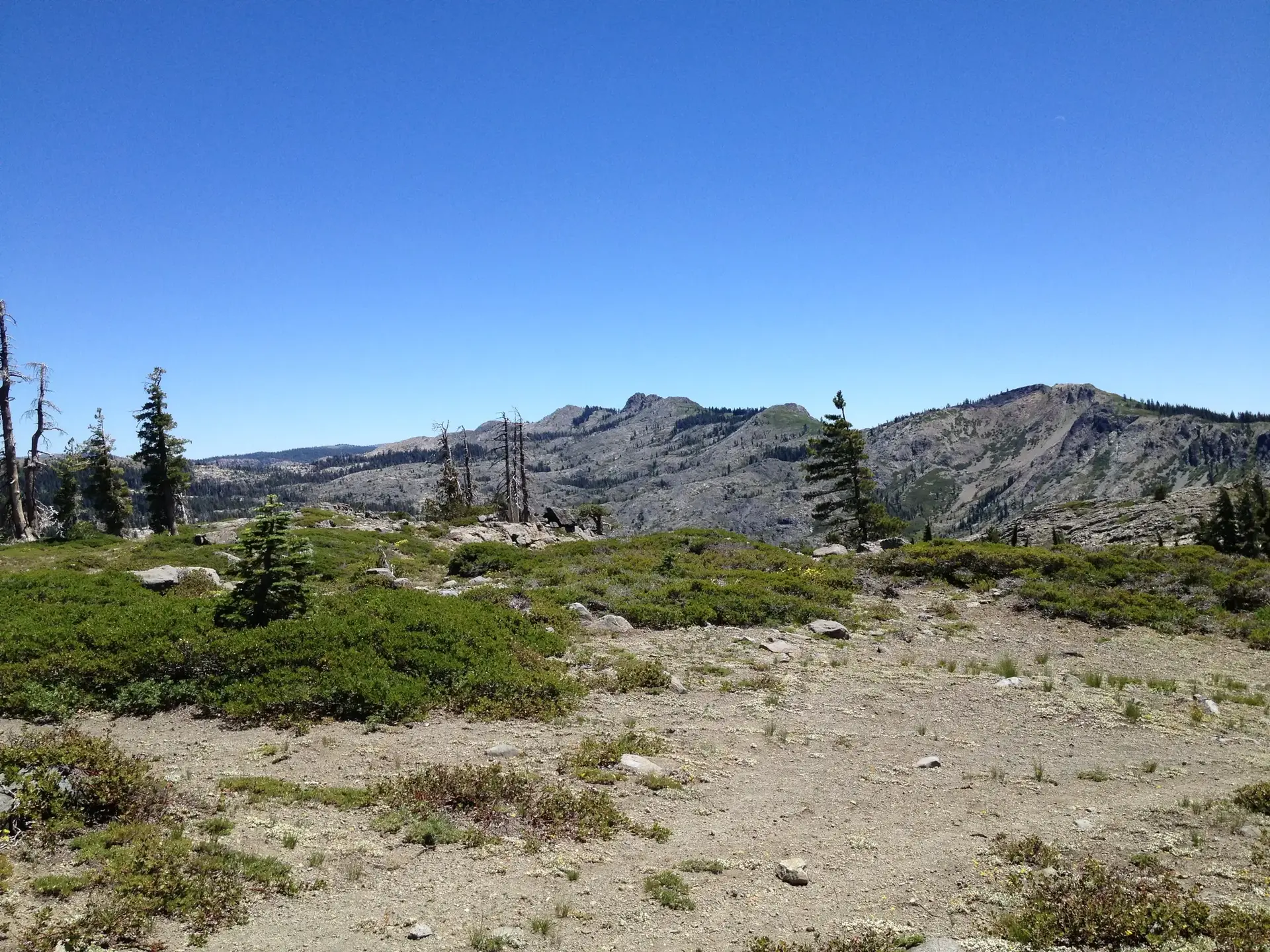 Expansive mountain landscape under a clear blue sky, with sparse vegetation.