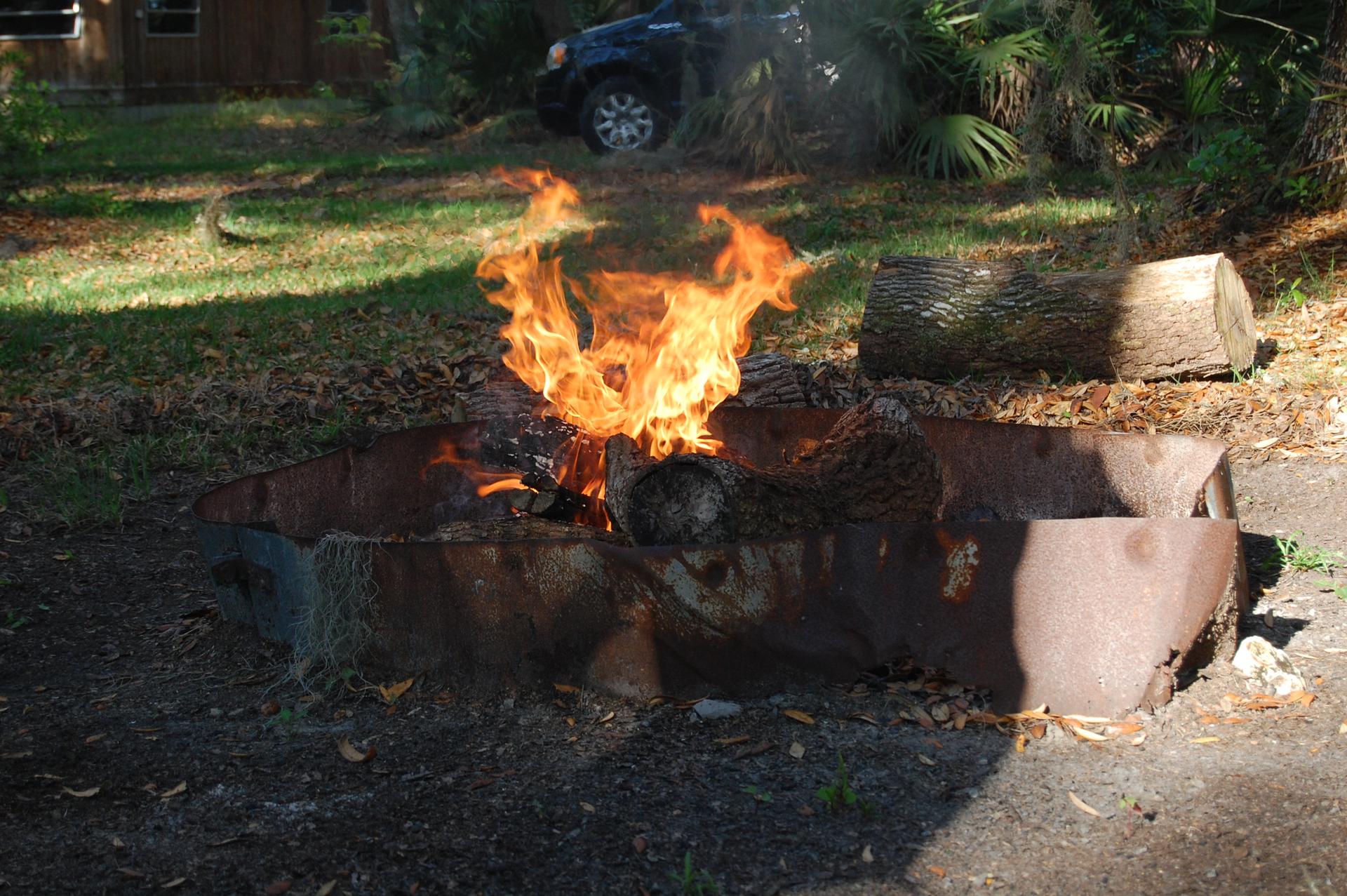 Bright orange flames burn in a rustic metal fire pit outdoors.